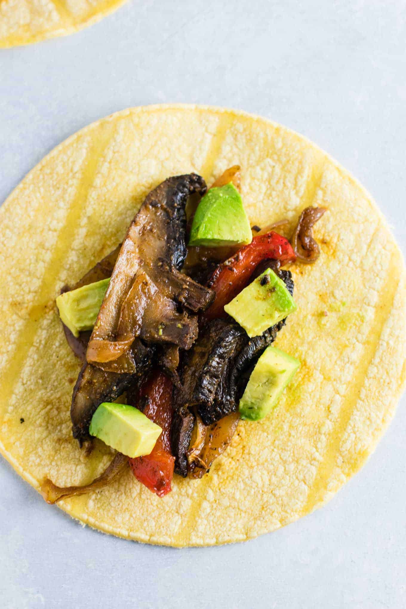 mushroom fajitas on a corn tortilla with diced avocado