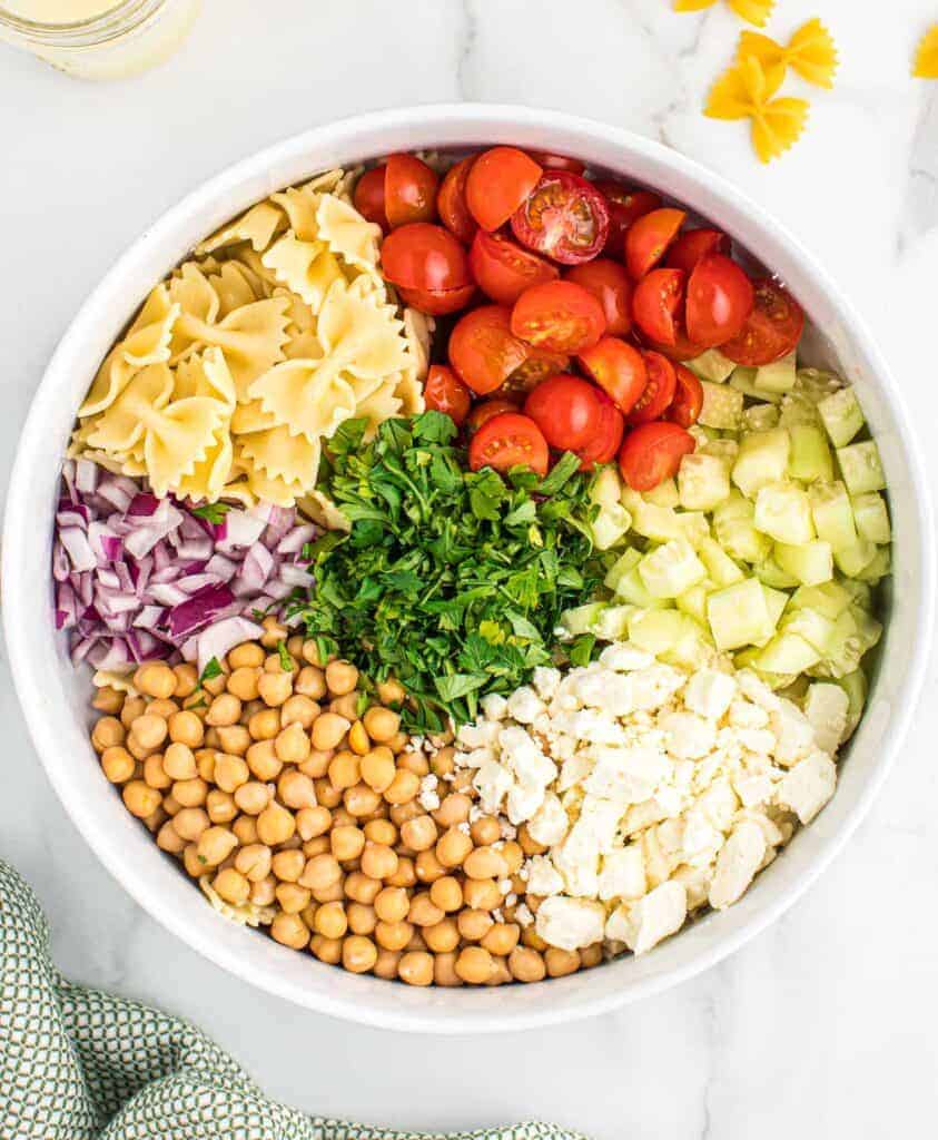 ingredients for pasta salad placed in groups in a mixing bowl
