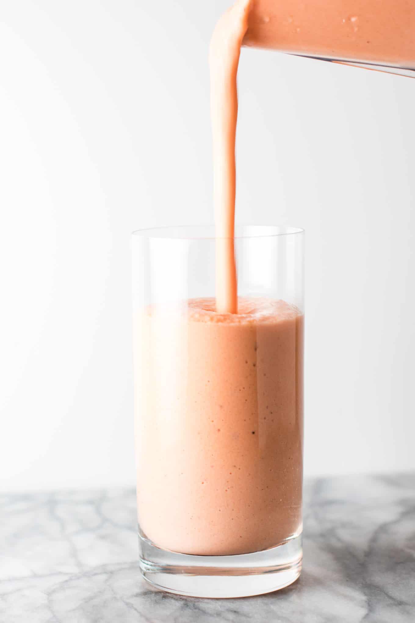 smoothie being poured into a glass from a blender, 3/4 of the way full