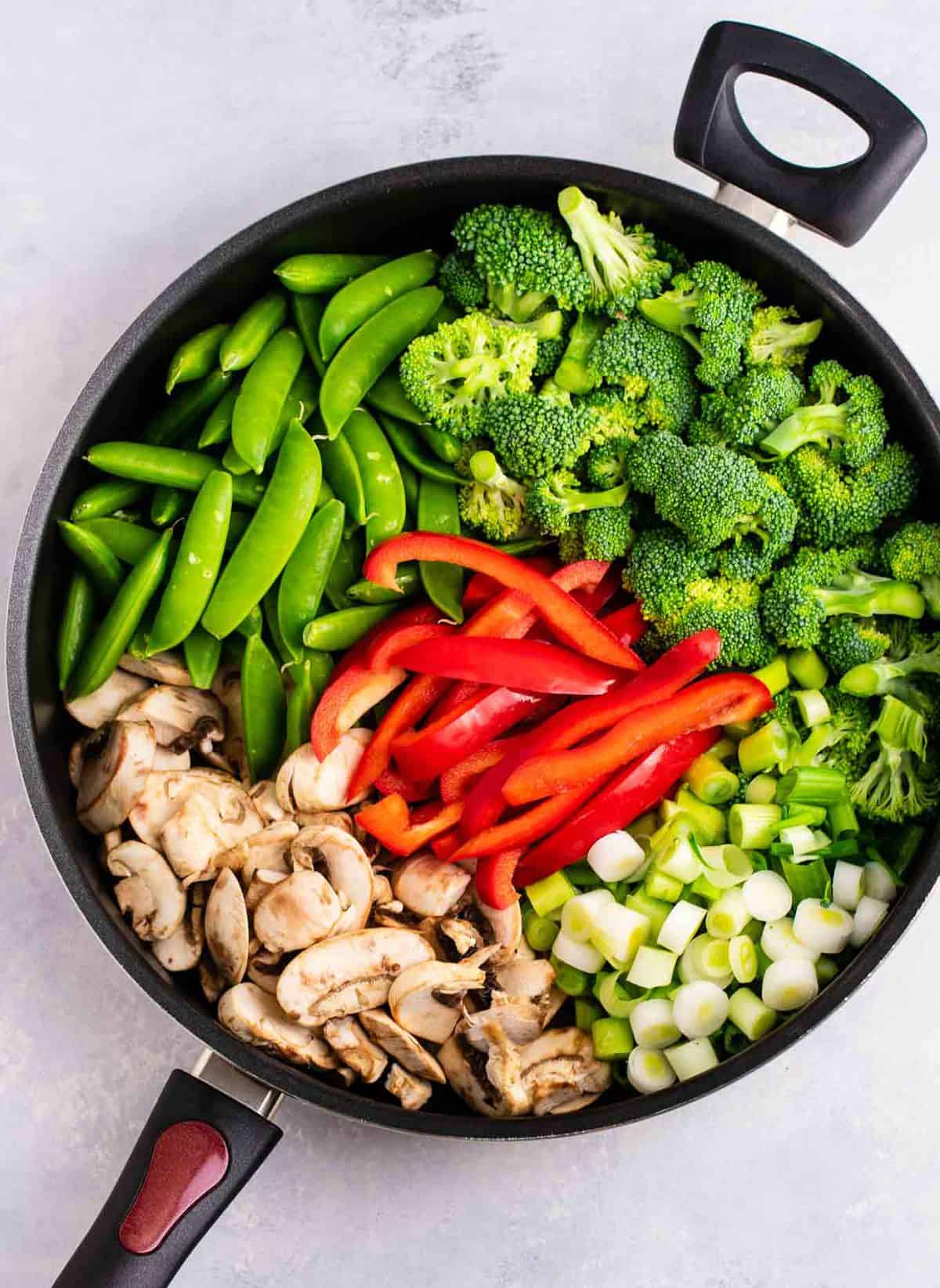 a skillet with stir fry veggies - snap peas, broccoli, red bell pepper, green onion, and sliced mushrooms