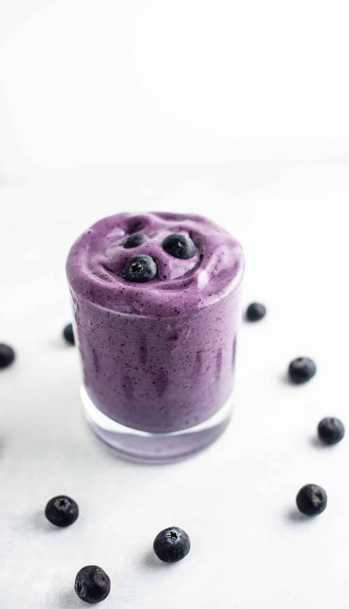 Blueberry banana smoothie in a glass with fresh blueberries around it