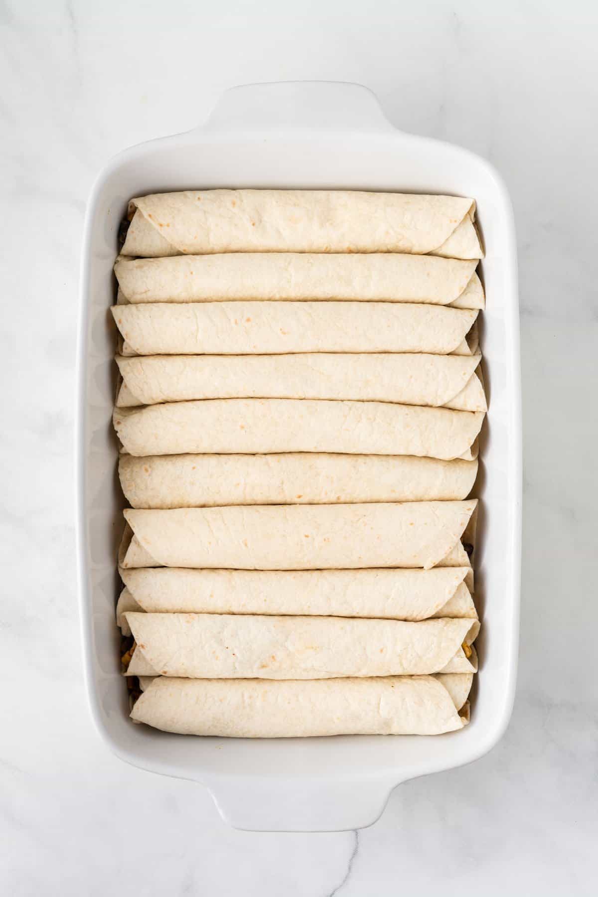 large baking dish filled with rolled up enchiladas