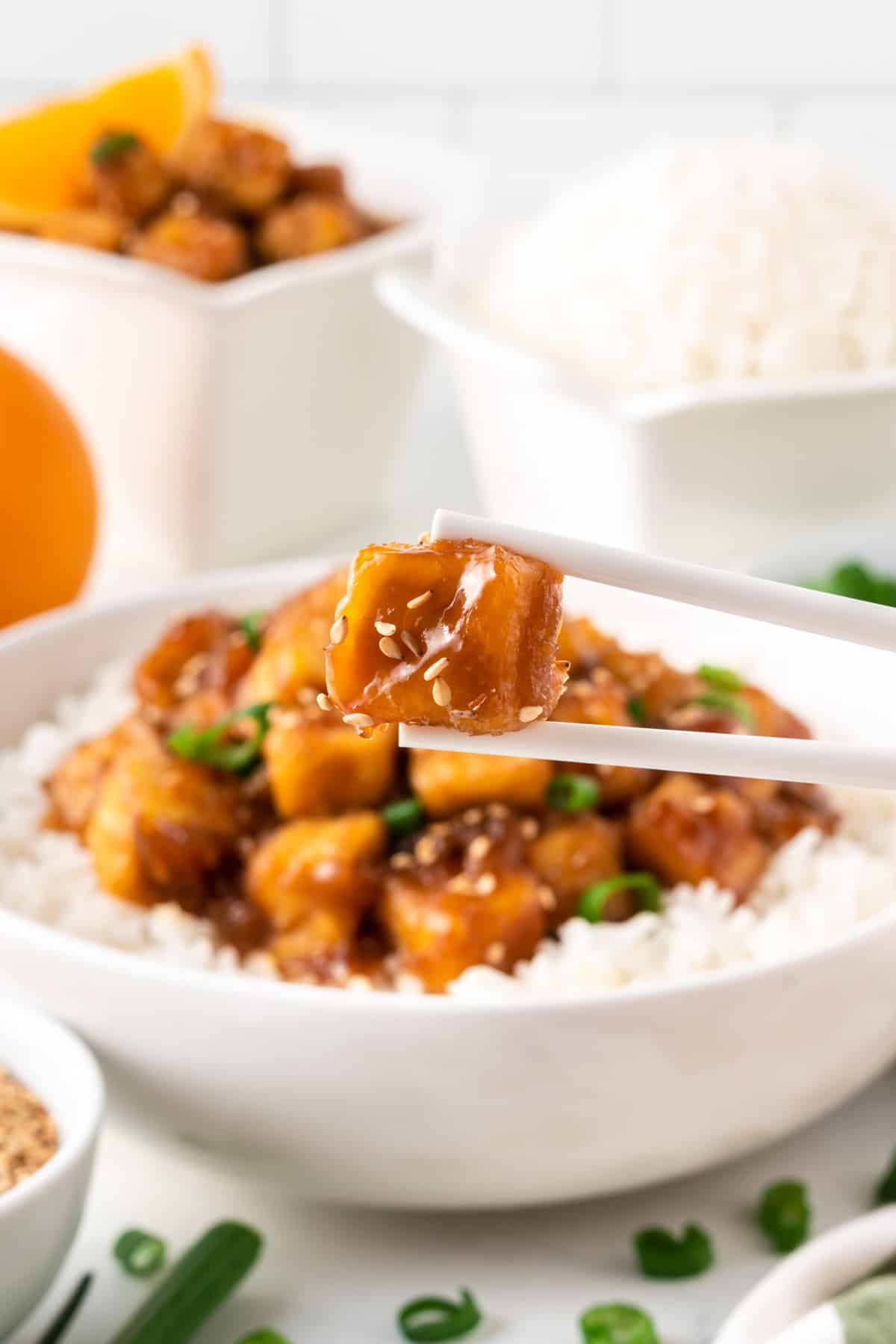 chopsticks holding a piece of orange tofu