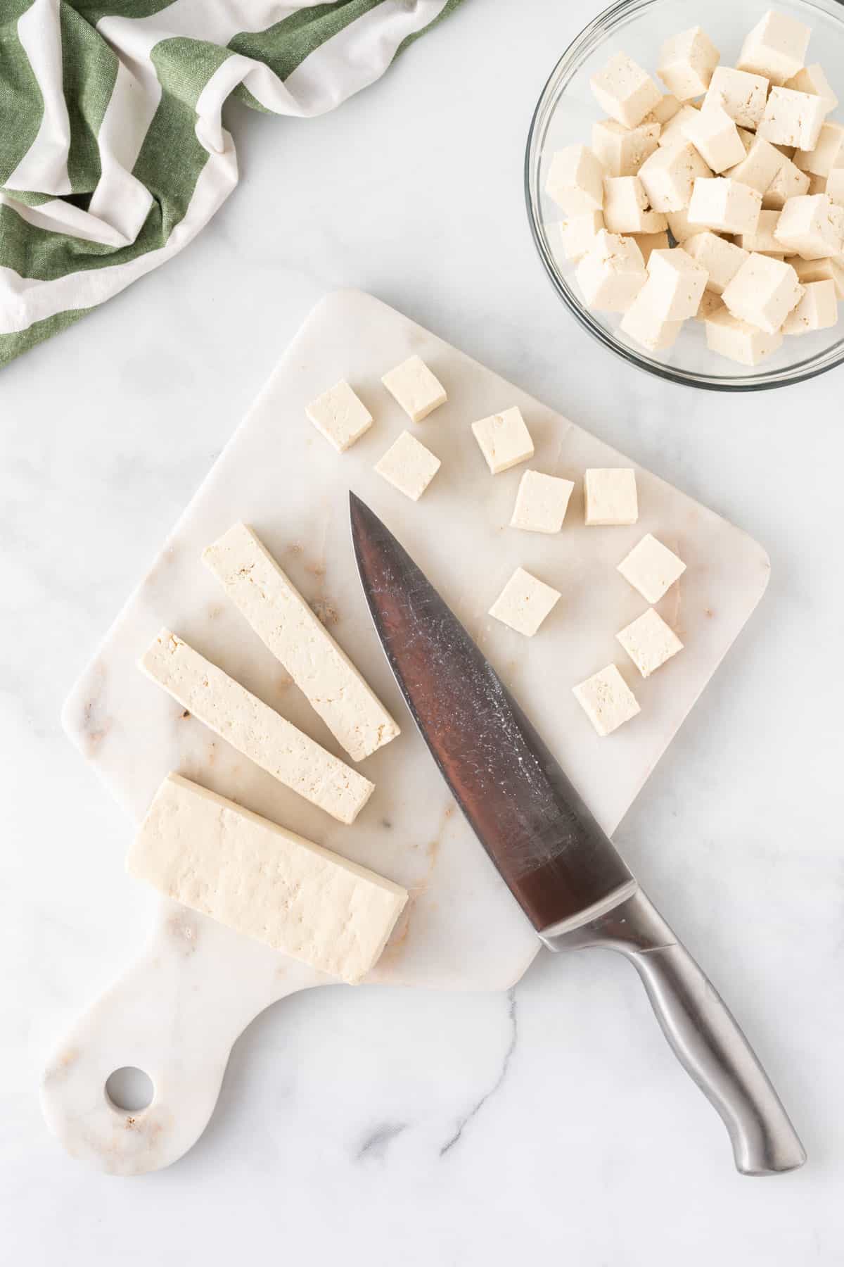 cutting tofu into cubes on a cutting board