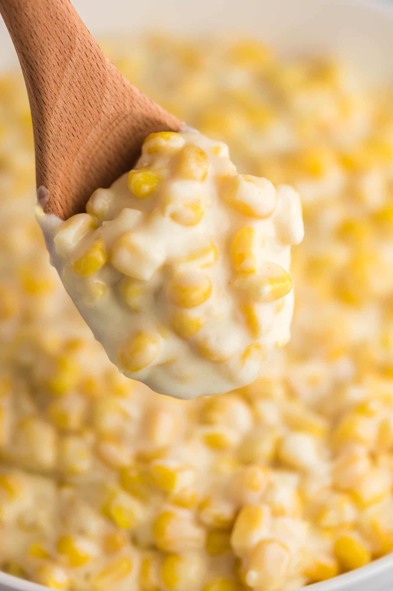 a wooden spoon taking a scoop of creamed corn