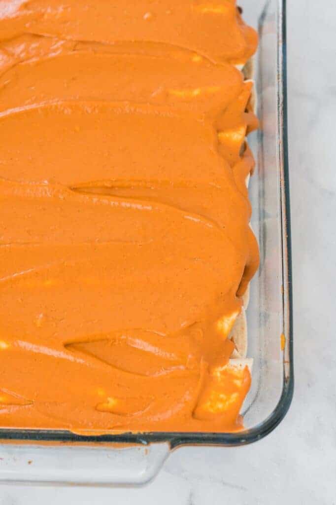 enchiladas rolled up in a casserole dish and topped with cashew queso