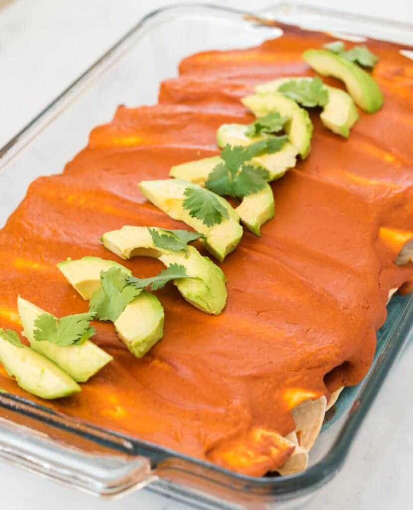 baked vegan enchiladas topped with sliced avocado and cilantro