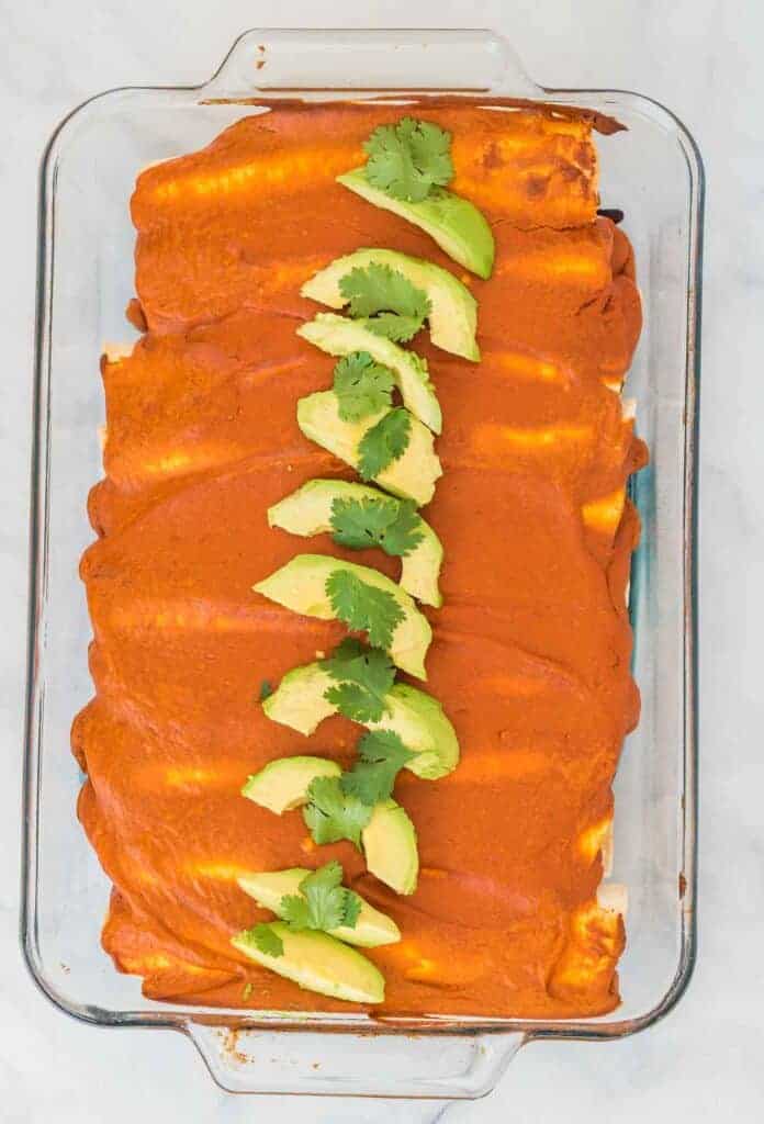 baked vegan enchiladas topped with sliced avocado and cilantro