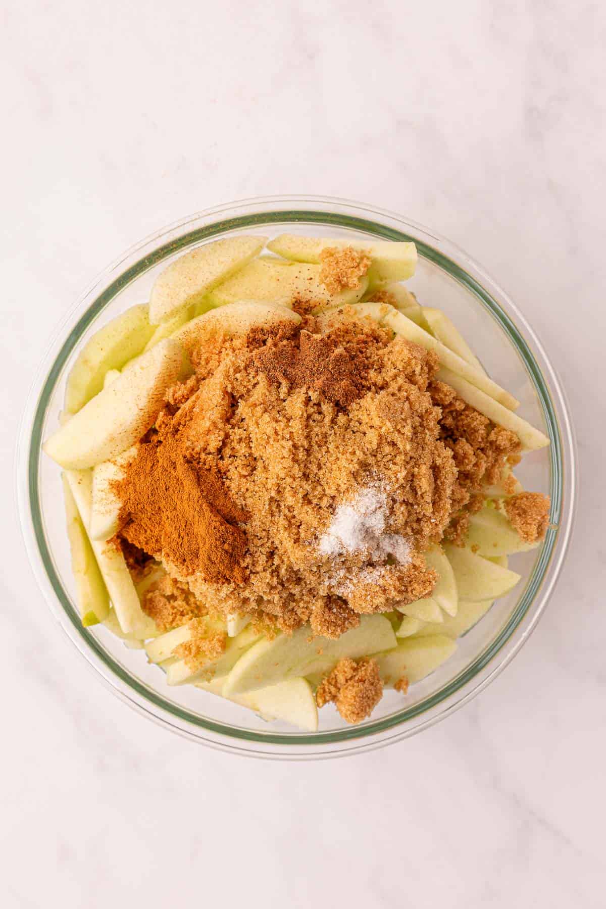 spices added to sliced apples in a mixing bowl