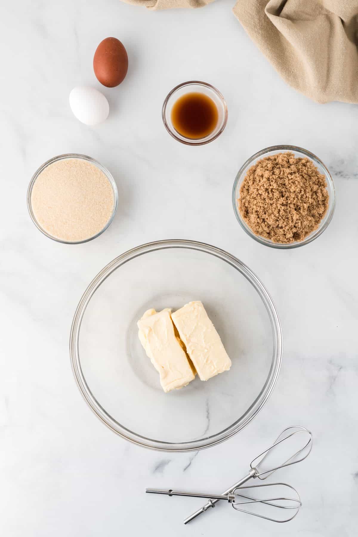 butter in a bowl surrounded by the sugar, eggs, and vanilla extract