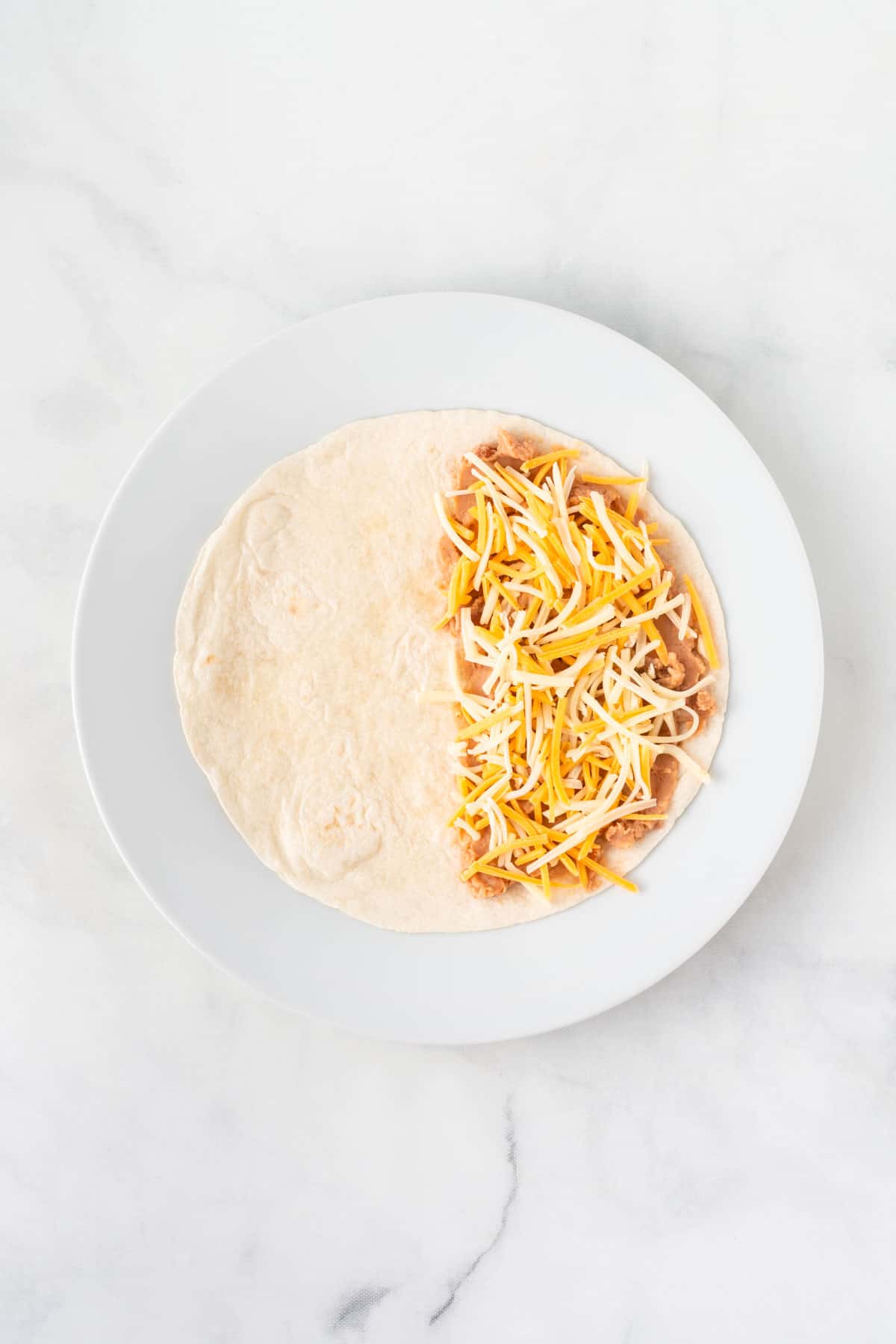 soft taco shell half spread with refried beans and mexican cheese