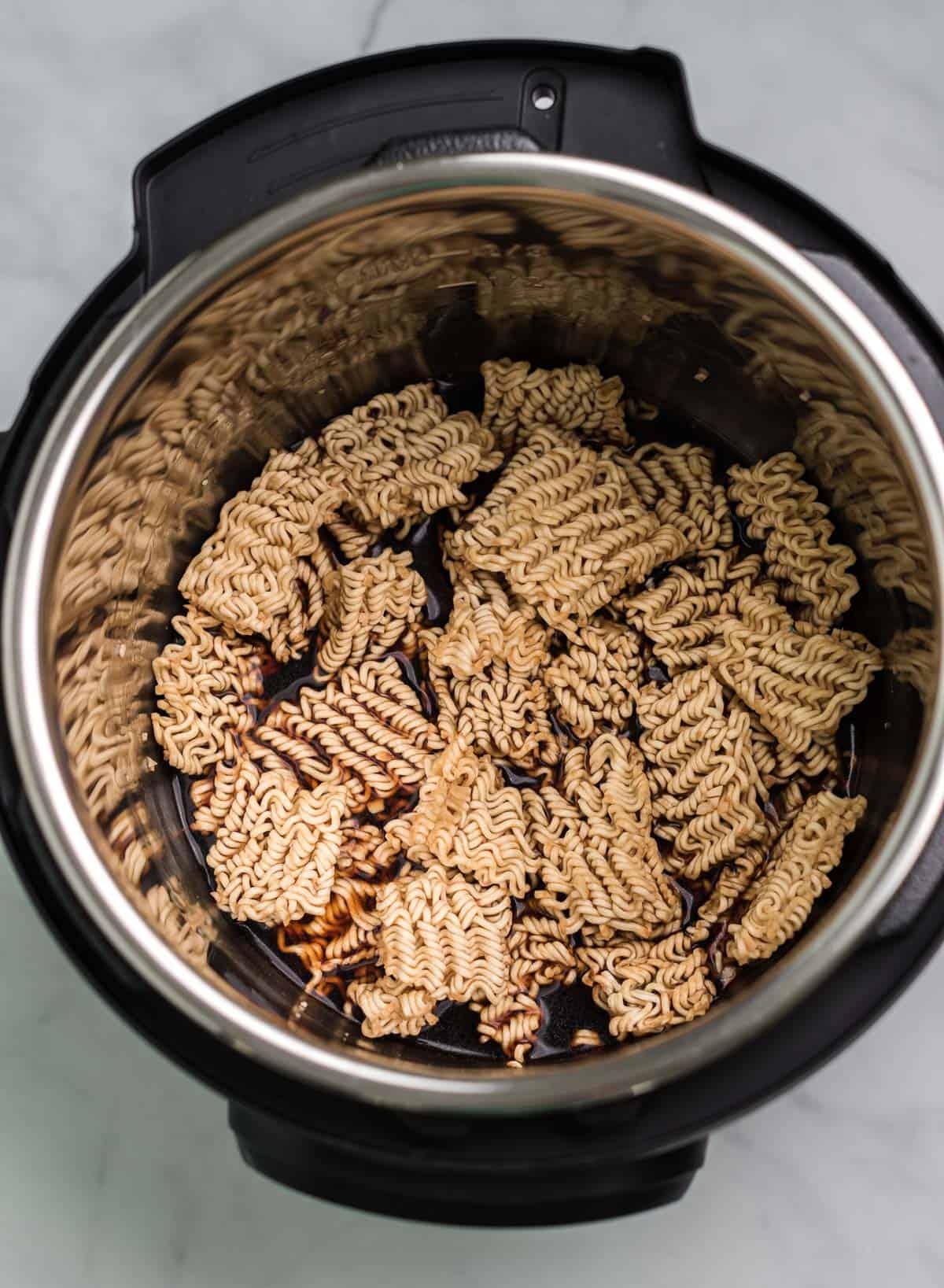 adding soy sauce and vegetable broth to the ramen noodles