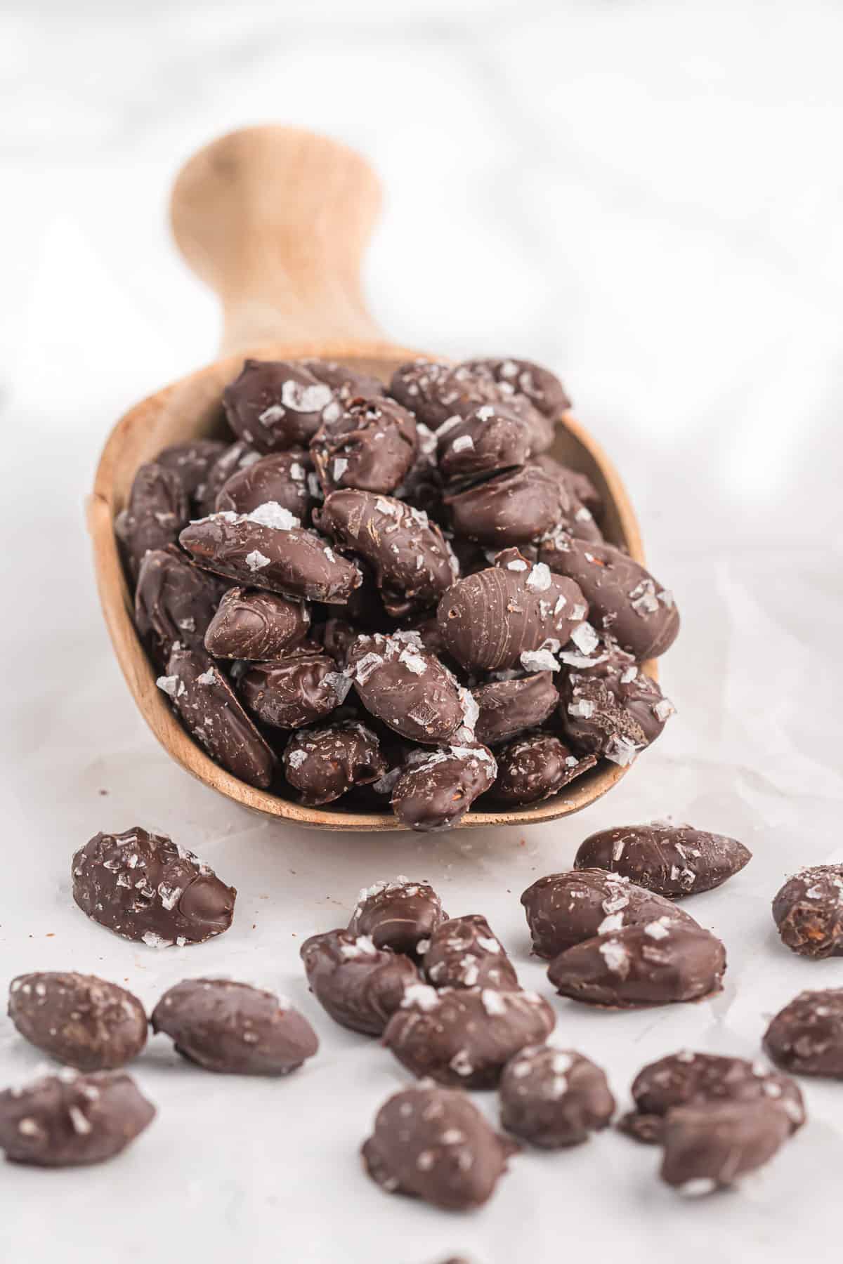 a wooden scoop of chocolate covered almonds