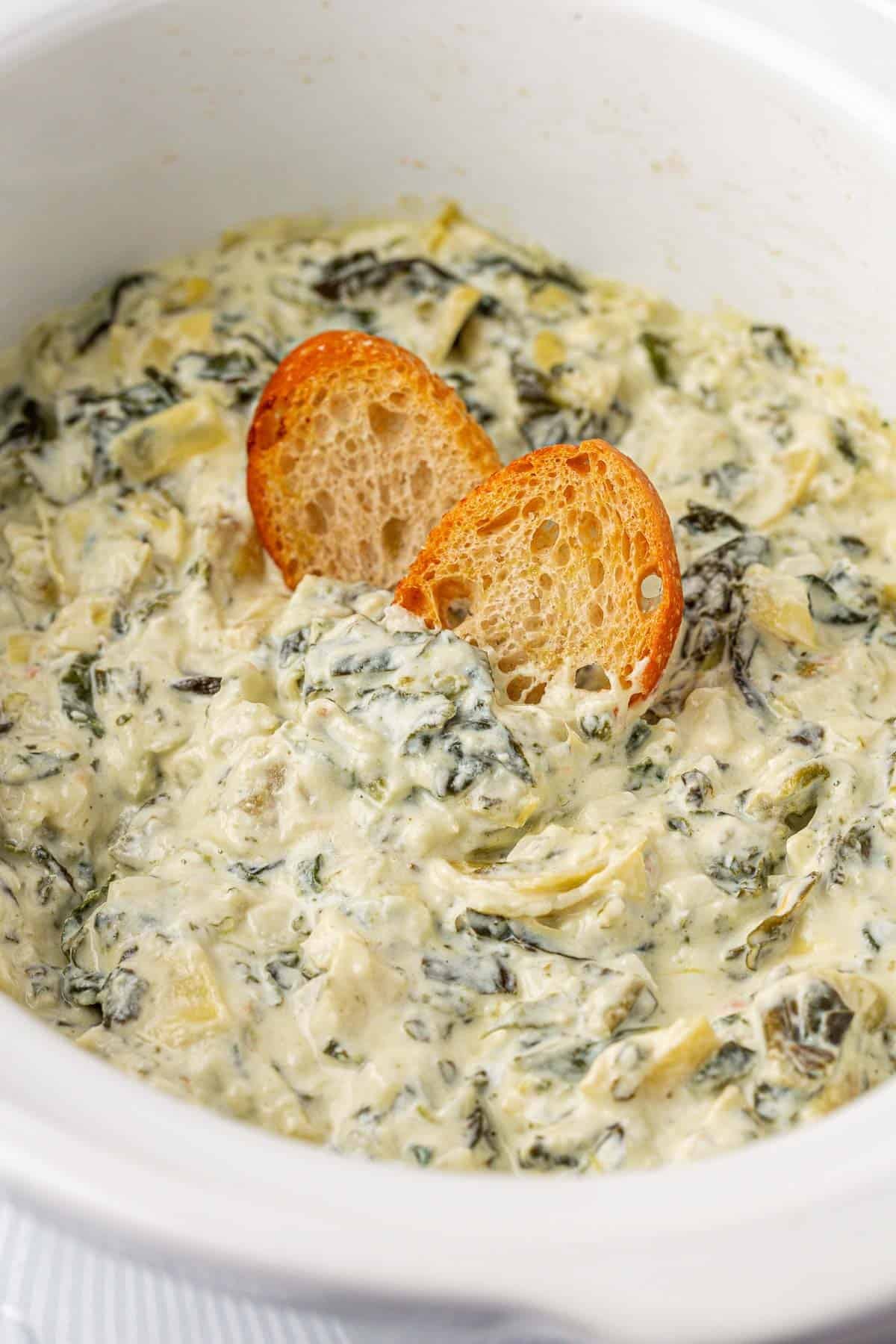 crock pot spinach artichoke dip with baguette slices in it