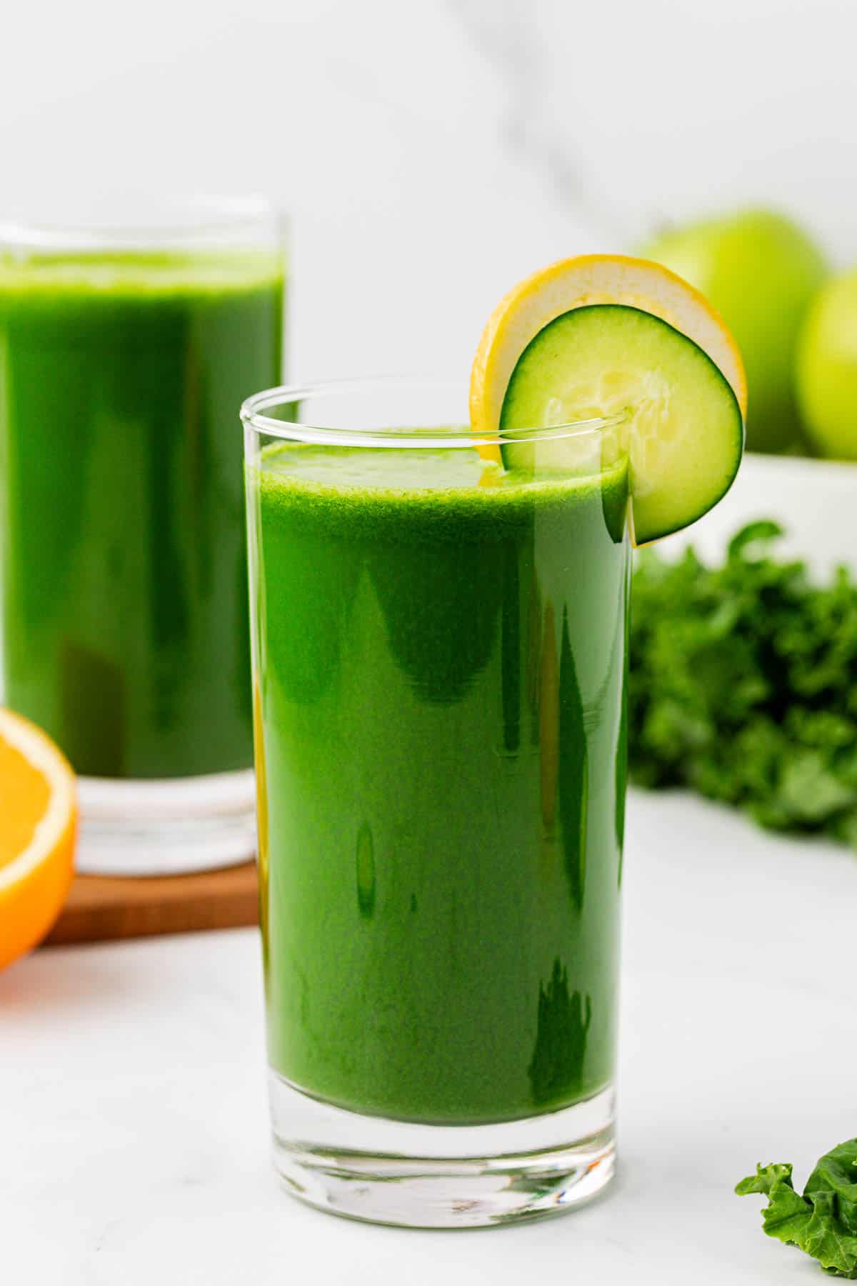 kale juice in a glass with a lemon and cucumber slice on the rim
