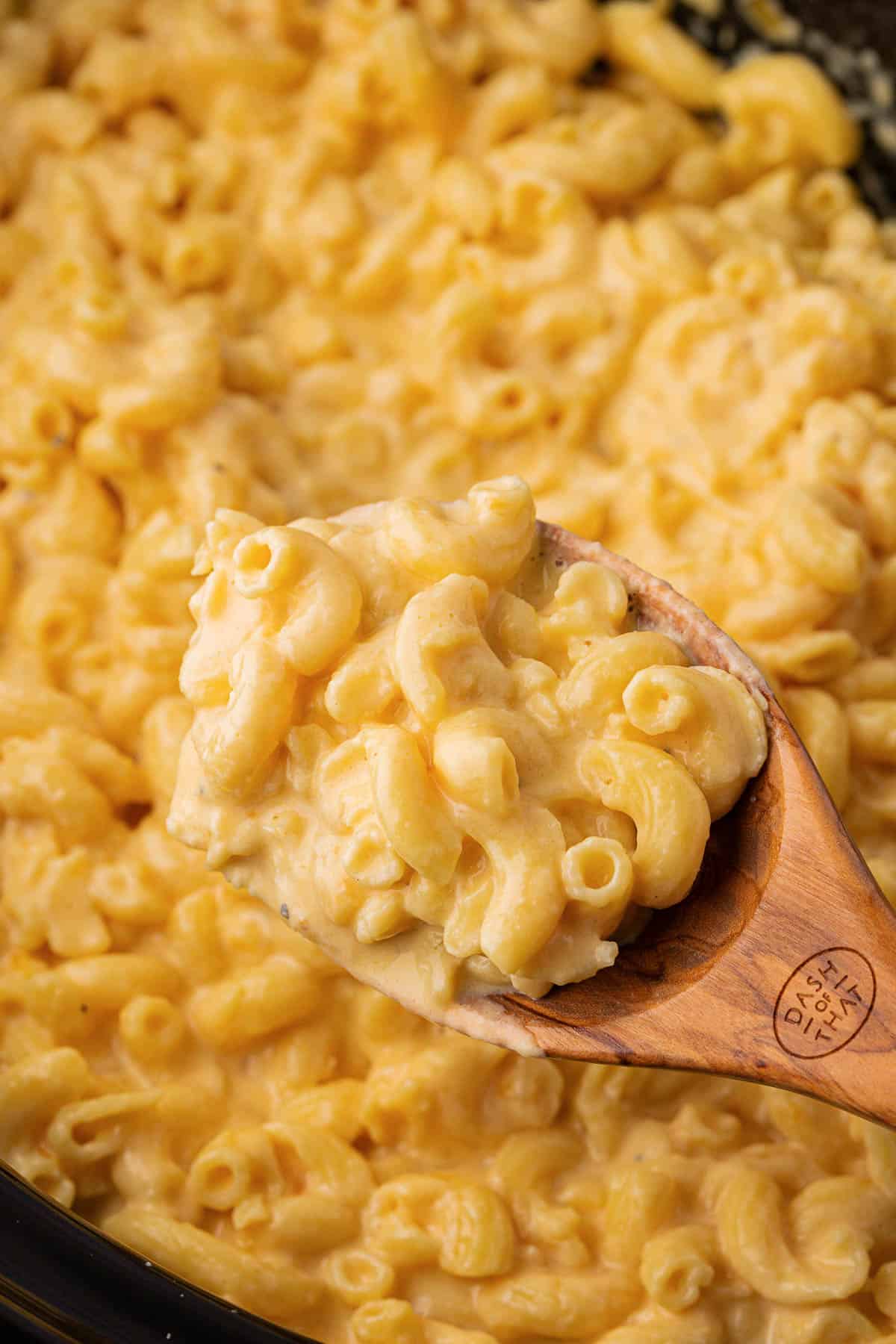 a wooden spoon taking a scoop of mac and cheese from the crock pot