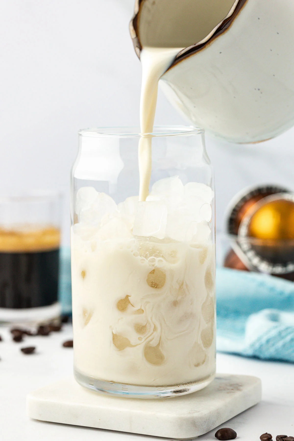 pouring oat milk into a glass filled with ice