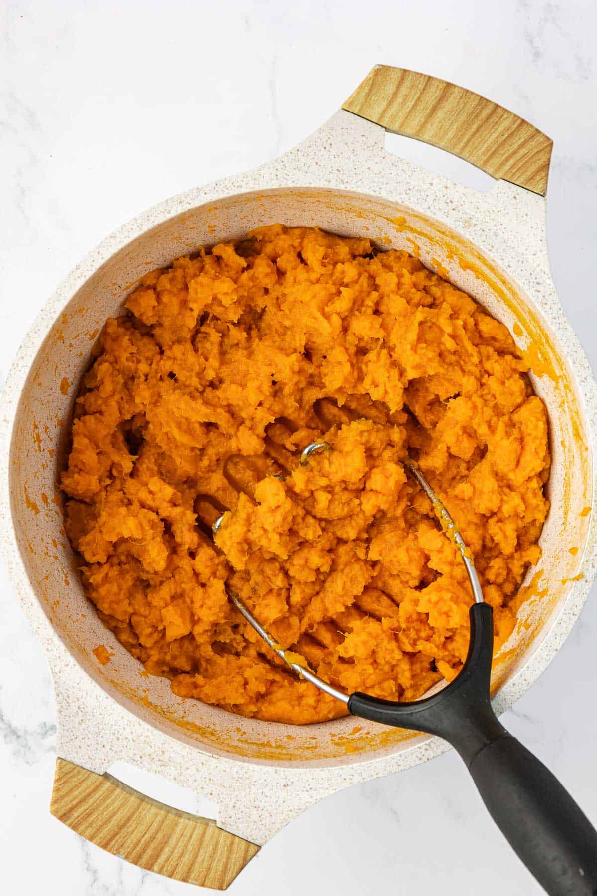mashing sweet potatoes in a pan