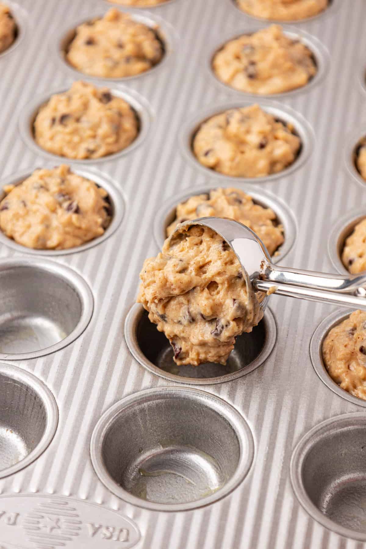 using a mini cookie scoop to fill the mini muffin tin with batter