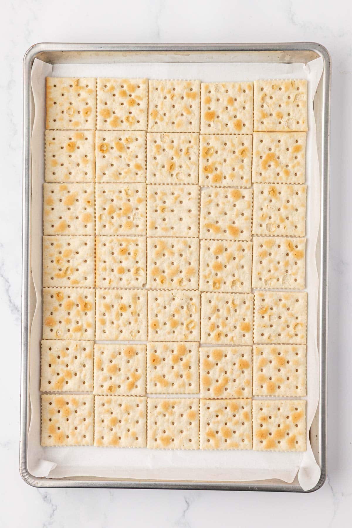saltine crackers lined up on a baking sheet