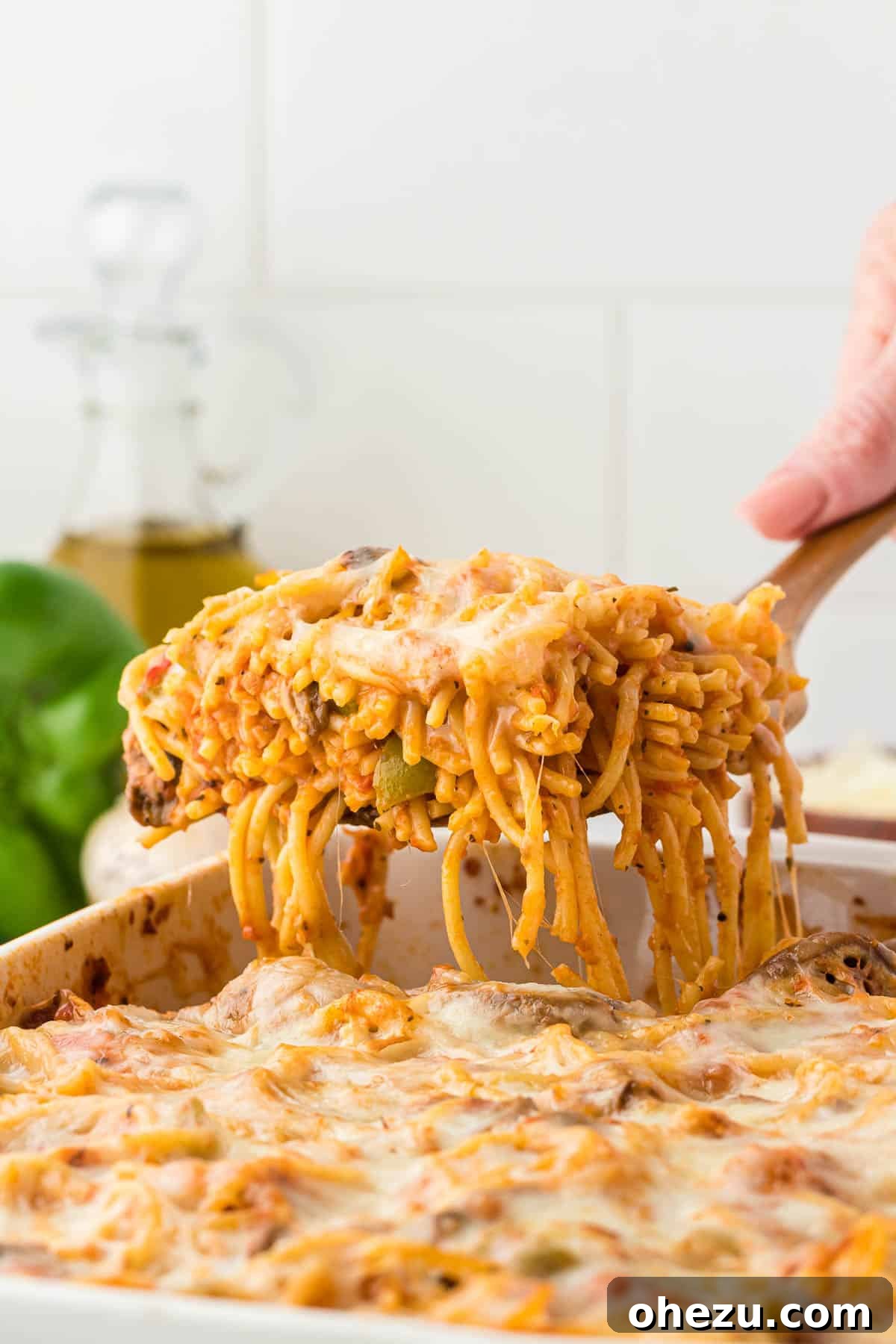 A serving of bubbly, golden-brown baked spaghetti being taken from a casserole dish, highlighting the melted cheese and rich sauce.