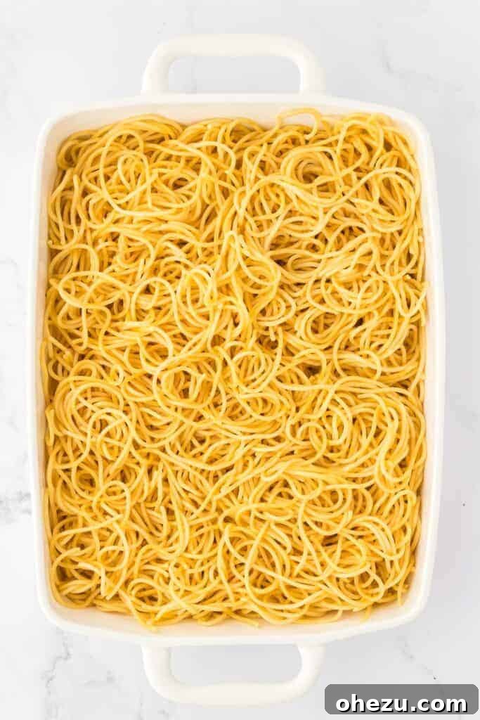 Cooked spaghetti laid out evenly in a rectangular casserole dish, forming the base layer.
