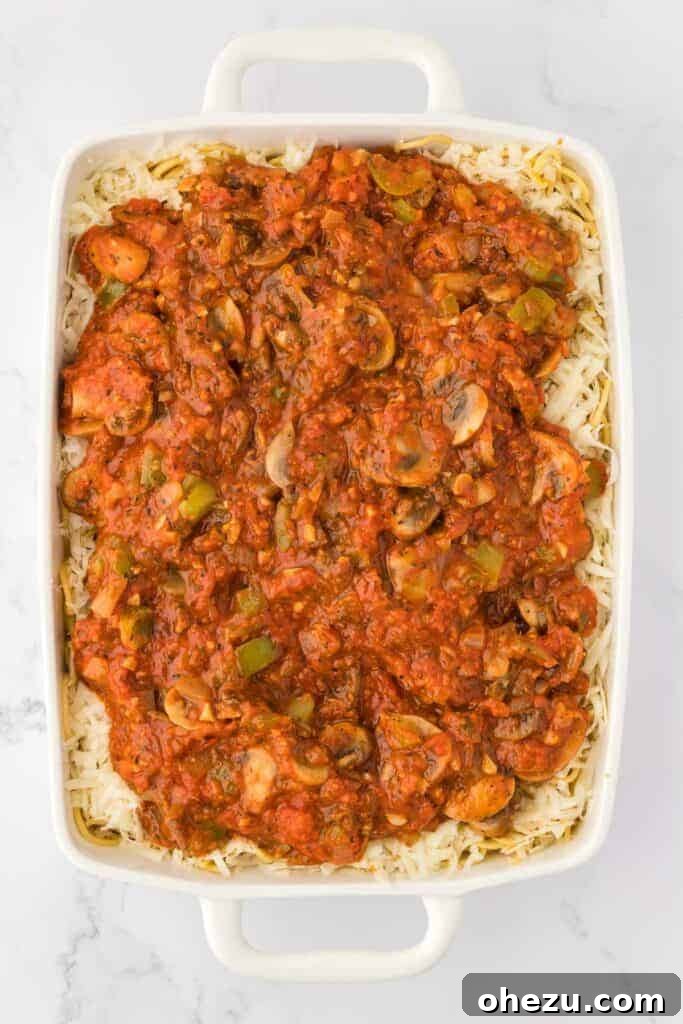 Vegetarian spaghetti sauce poured over the spaghetti and cheese mixture in the casserole dish.