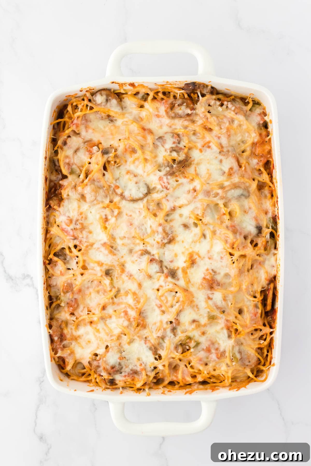 A freshly baked vegetarian spaghetti casserole, hot and bubbly with a golden-brown cheese topping, straight from the oven.