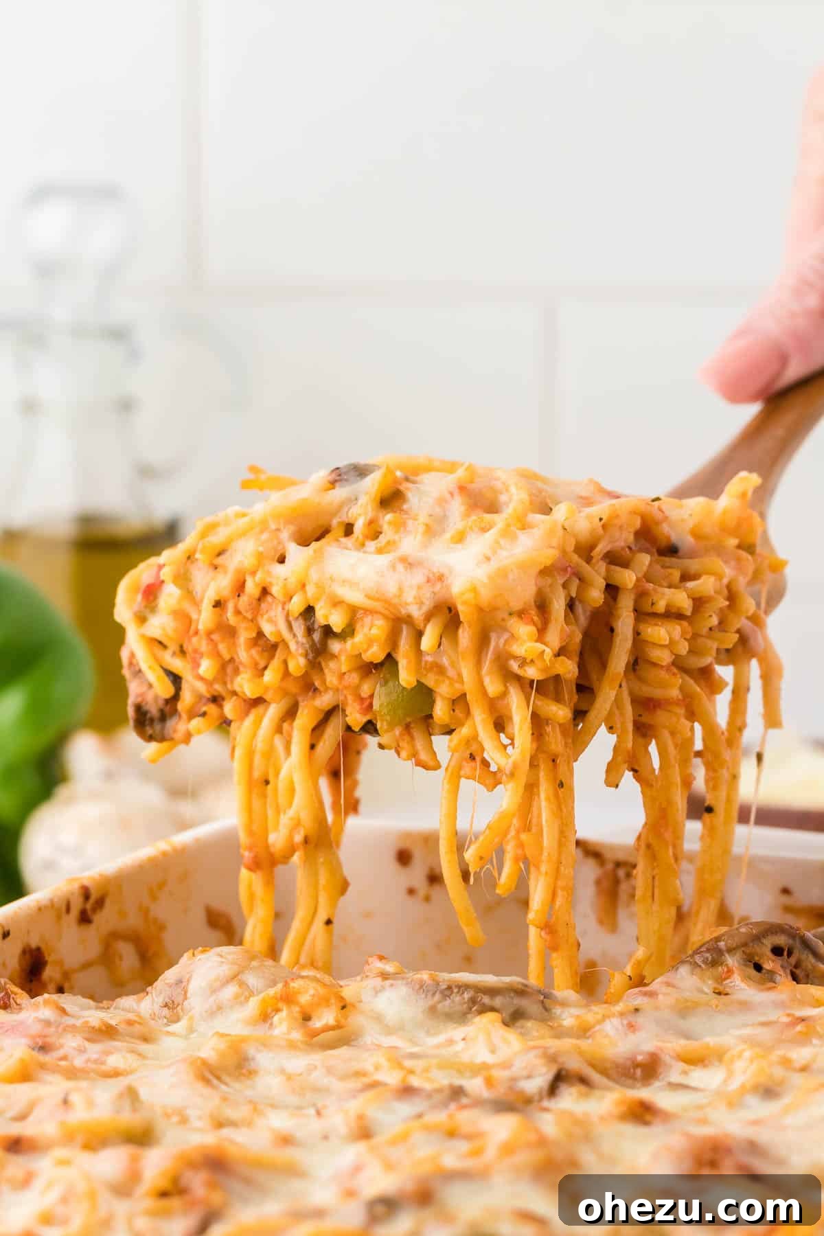 A serving of hot, cheesy baked spaghetti being lifted from the casserole dish with a serving spoon, ready to be placed on a plate.