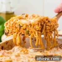 A serving of vegetarian baked spaghetti being taken from the dish, with a focus on the melted cheese and pasta.