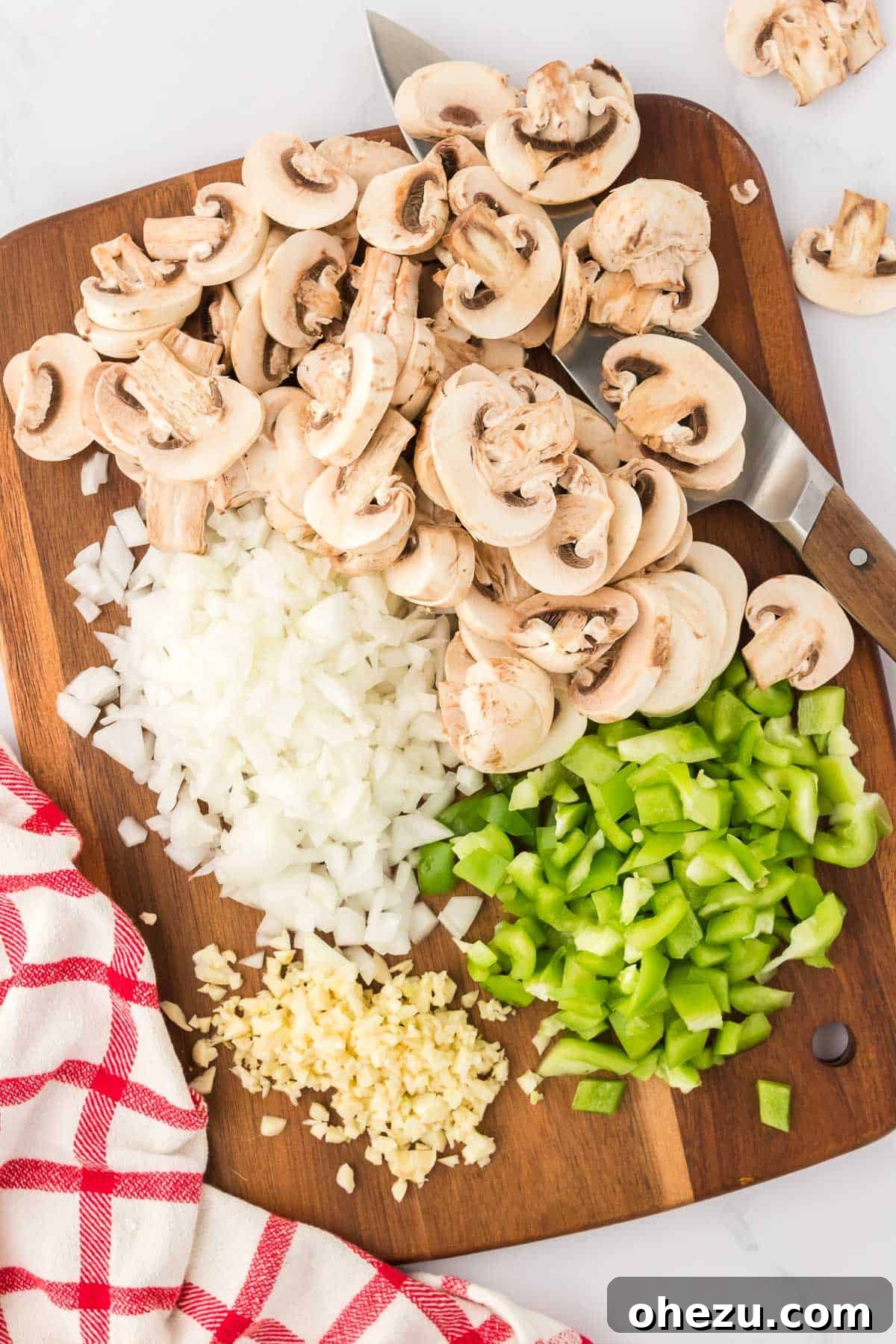 Finely chopped mushrooms, onion, green bell pepper, and minced garlic are neatly arranged on a cutting board, prepared for sautéing.