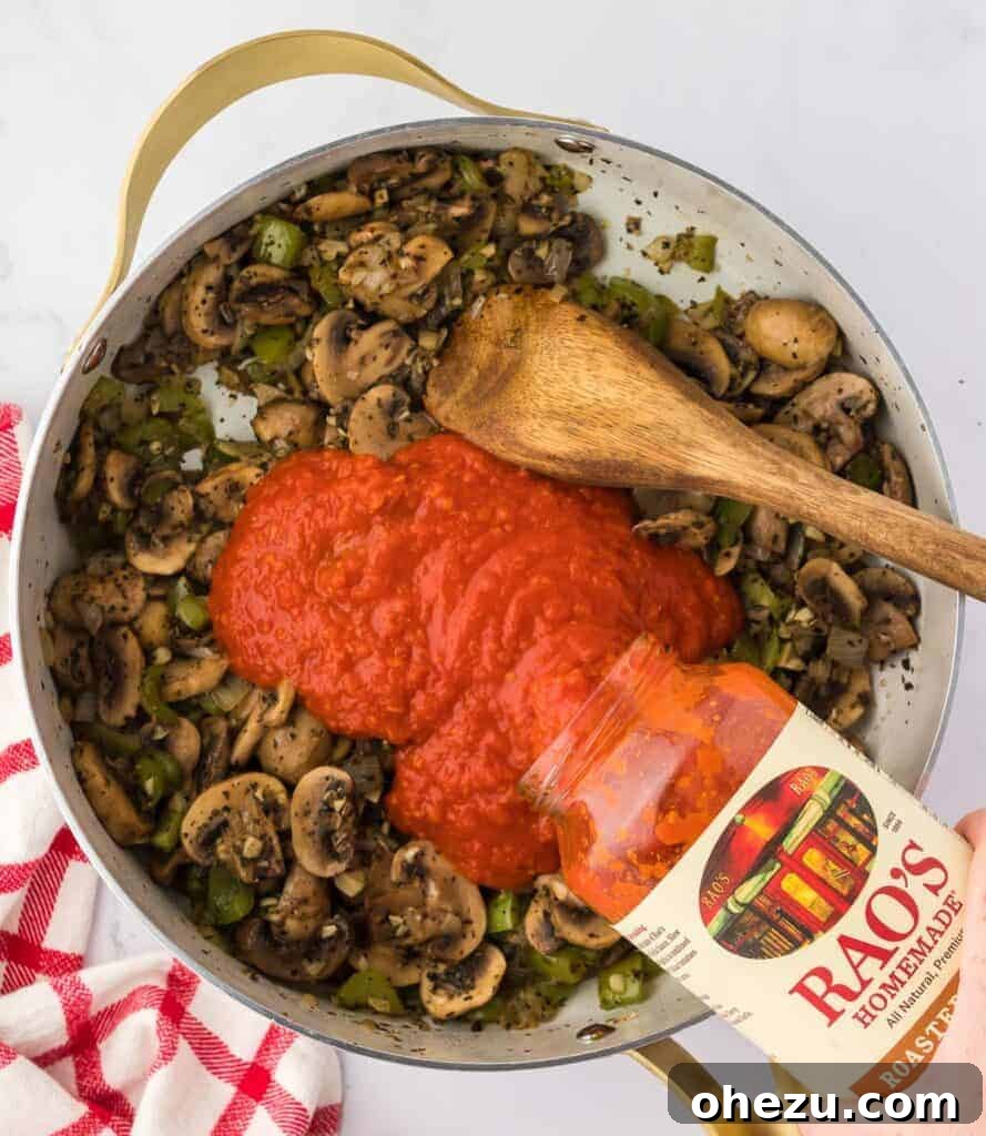 Pouring jarred pasta sauce over the sautéed vegetables in a large skillet.