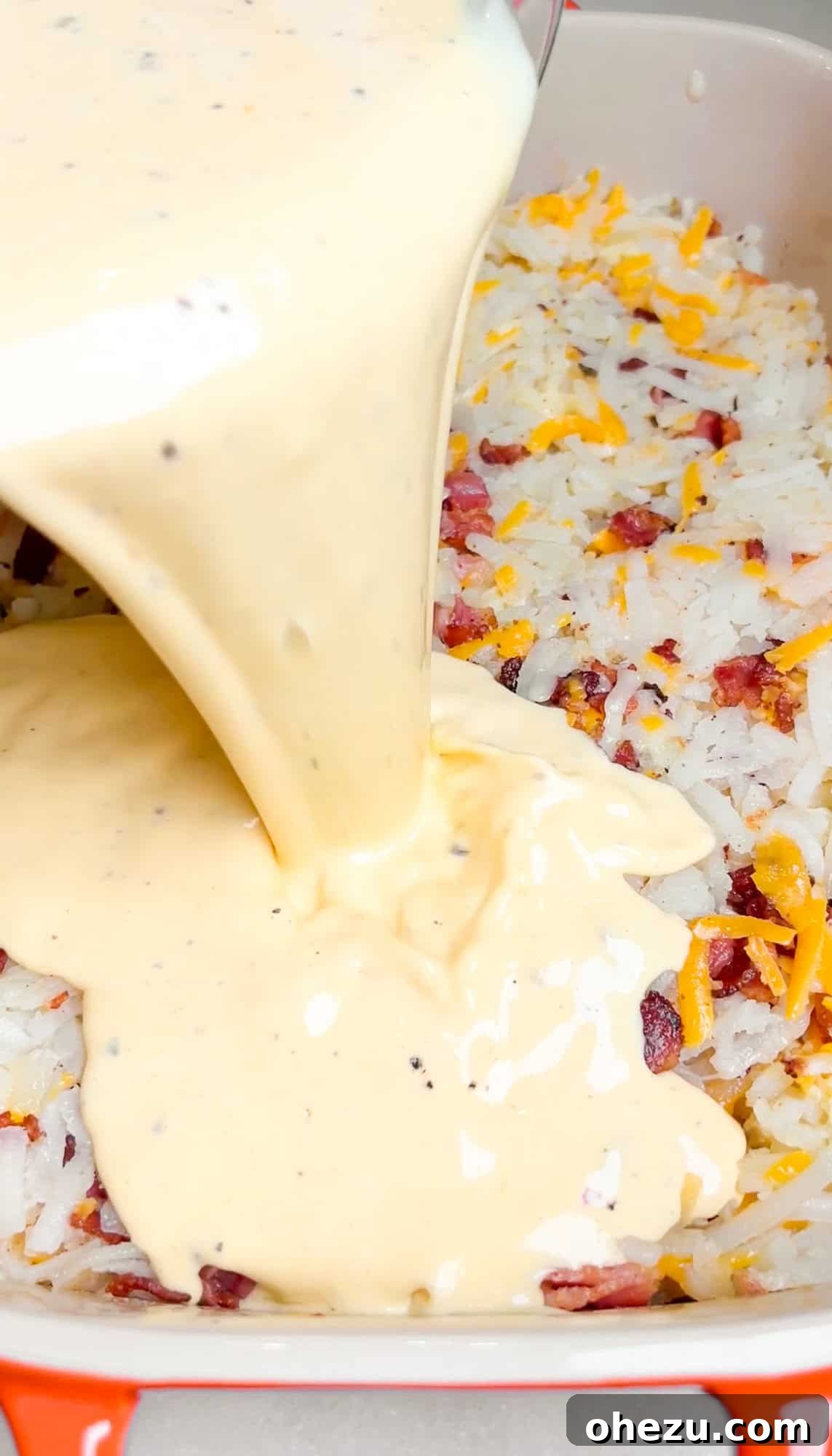 Pouring egg mixture evenly over hashbrowns, cheese, and bacon in a casserole dish