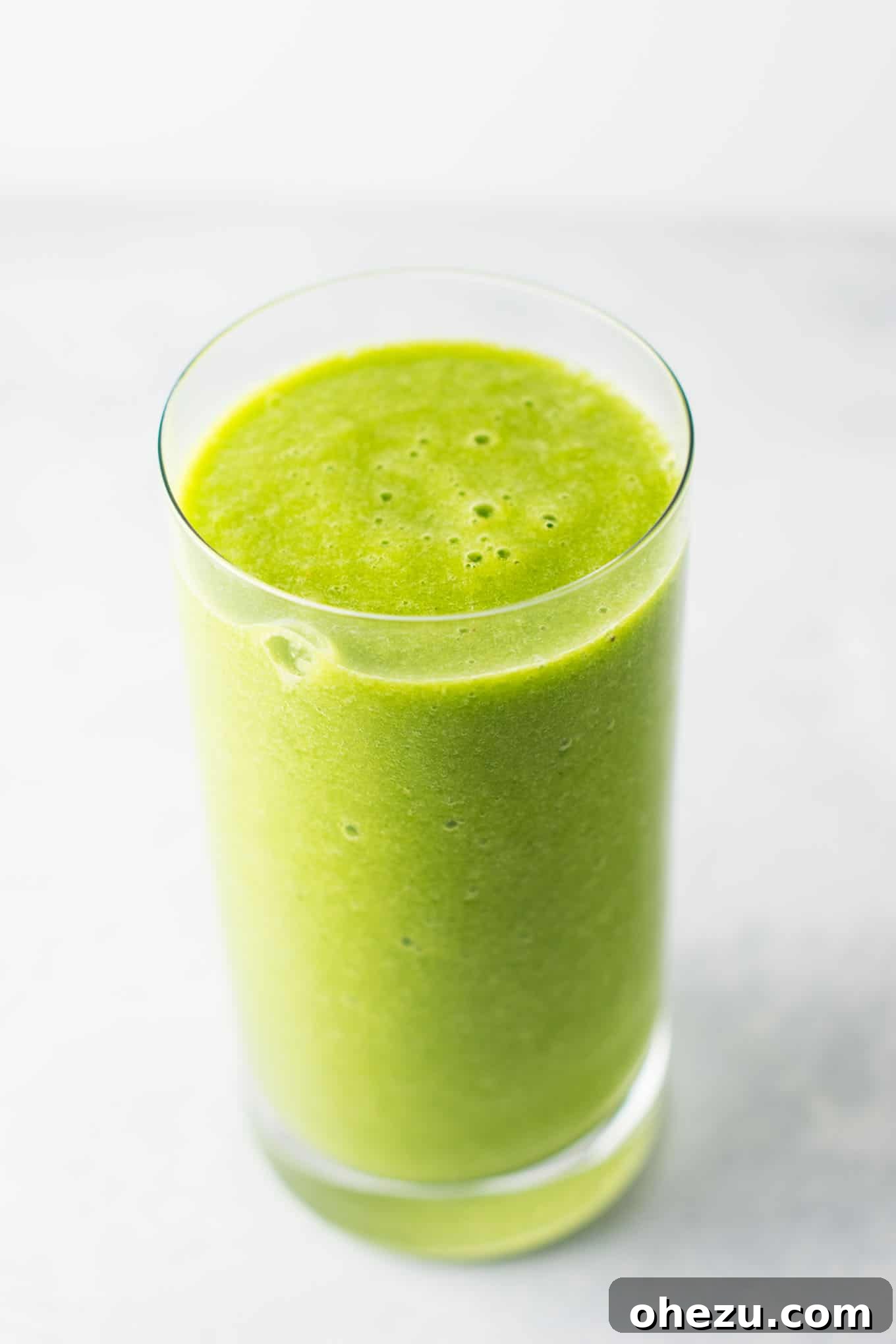 A vibrant green smoothie recipe made with kale, ginger, oranges, lemon, frozen banana, frozen peaches, and water
