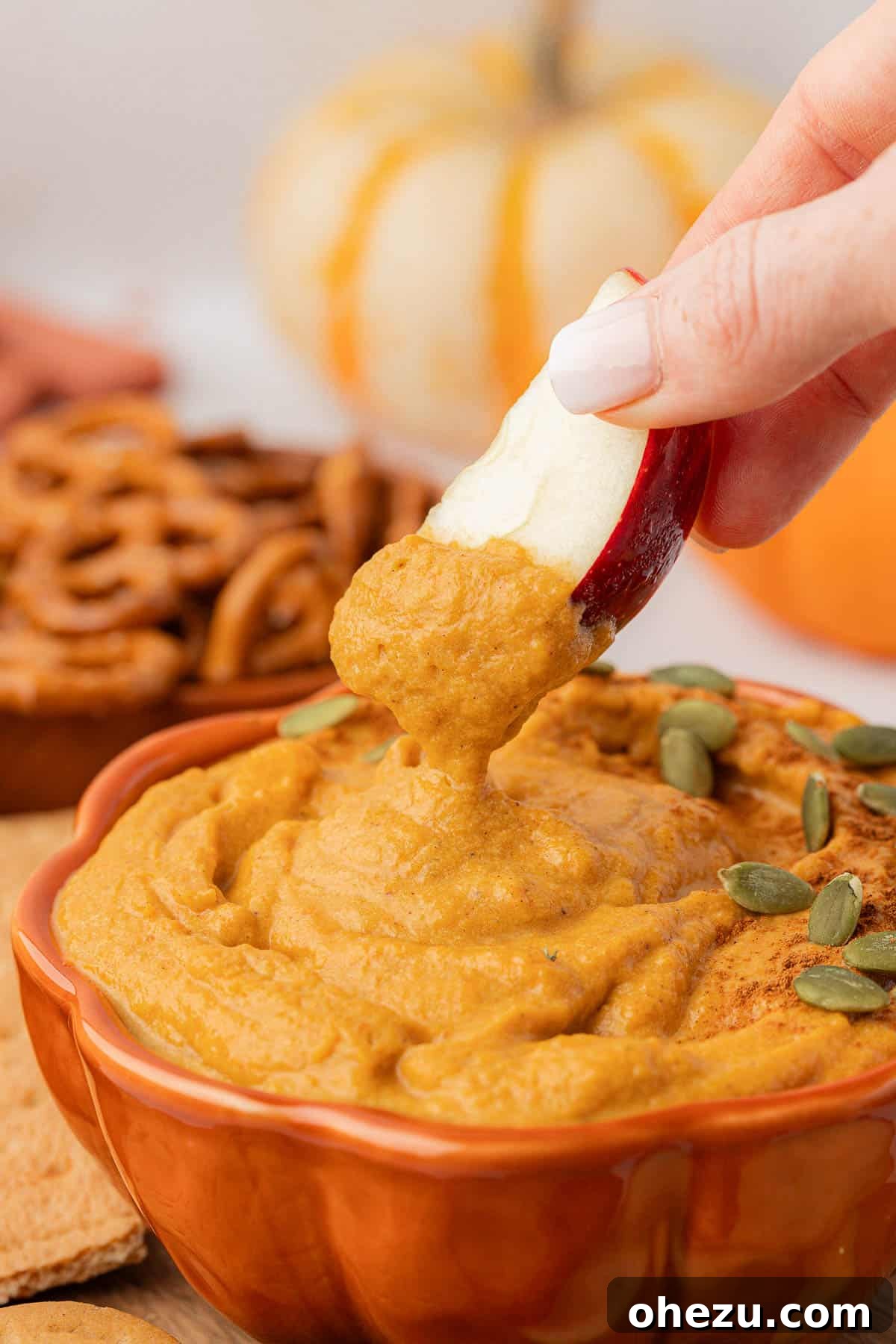 A hand dipping a crisp apple slice into the velvety pumpkin dip, showcasing its creamy texture