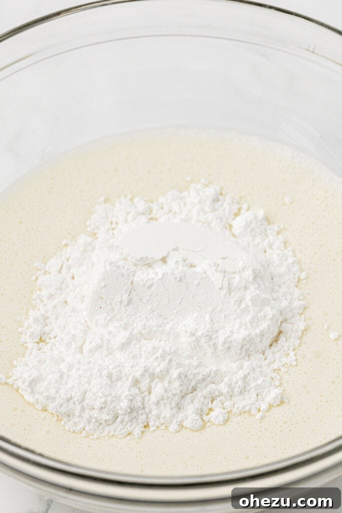 Pouring powdered sugar into cold heavy cream in a mixing bowl before whipping