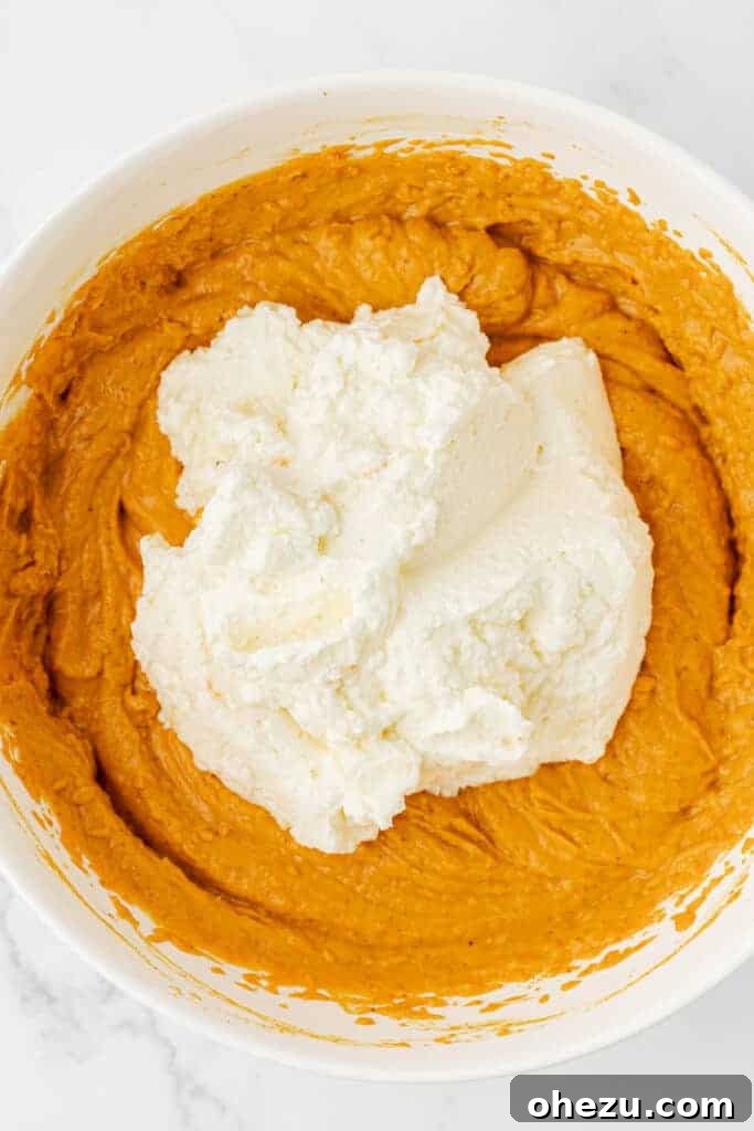 Gently folding the fluffy whipped cream into the pumpkin and cream cheese mixture