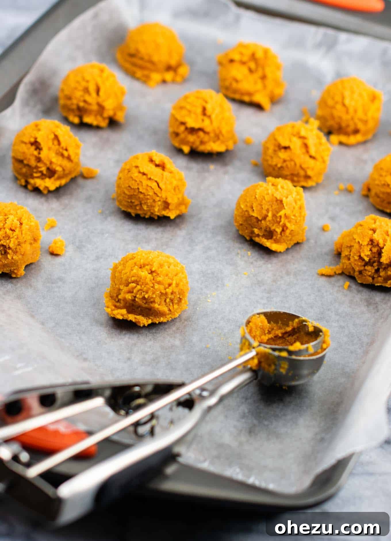Scoops of pumpkin truffle dough neatly arranged on a wax paper-lined baking sheet, ready for chilling.