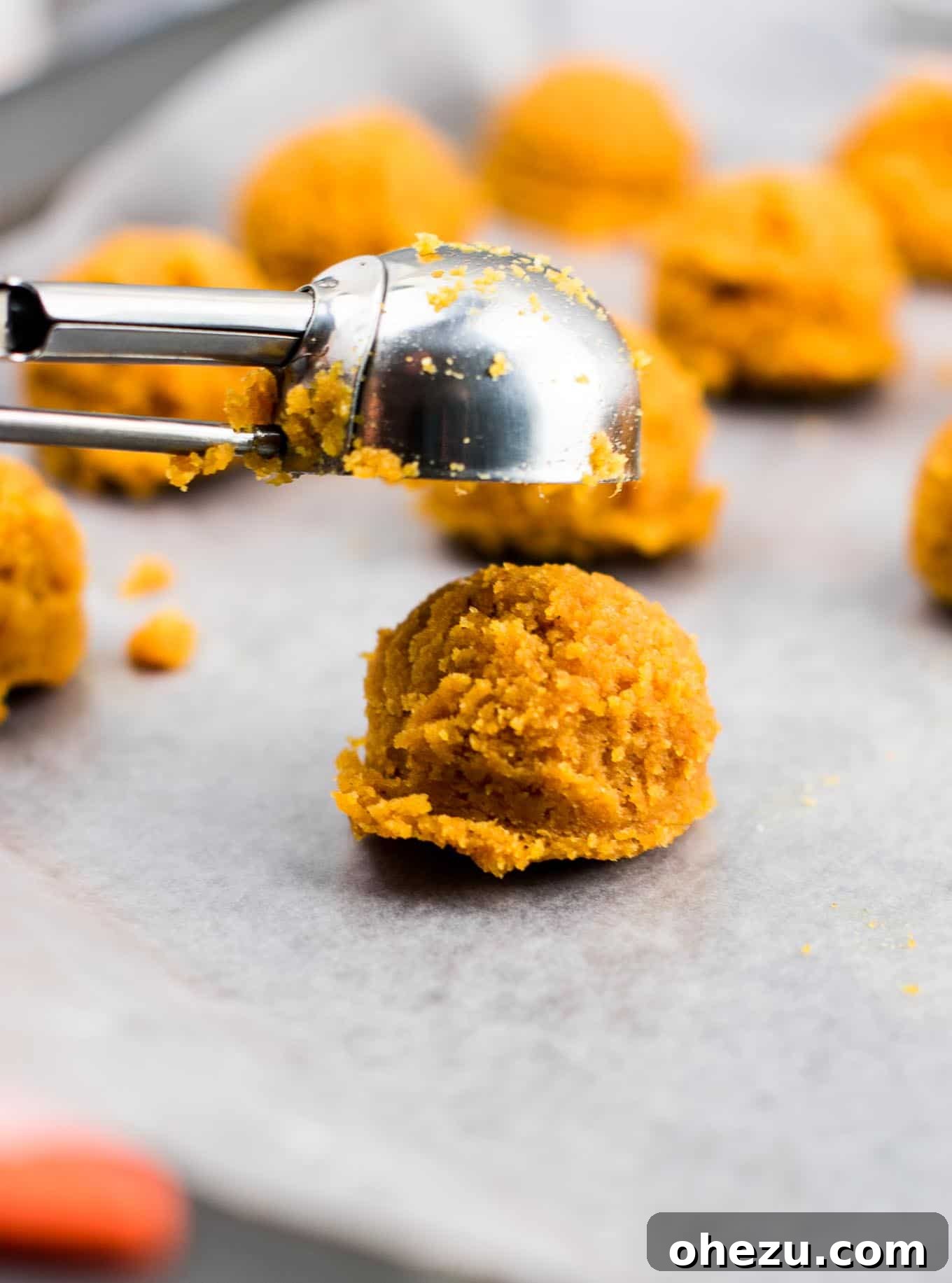 A mini cookie scoop being used to drop truffle dough onto a baking sheet, demonstrating the shaping process.