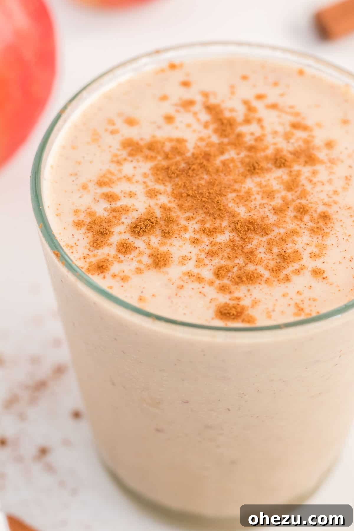 A beautifully presented glass of healthy apple pie smoothie with cinnamon and fresh apple slices as garnish.