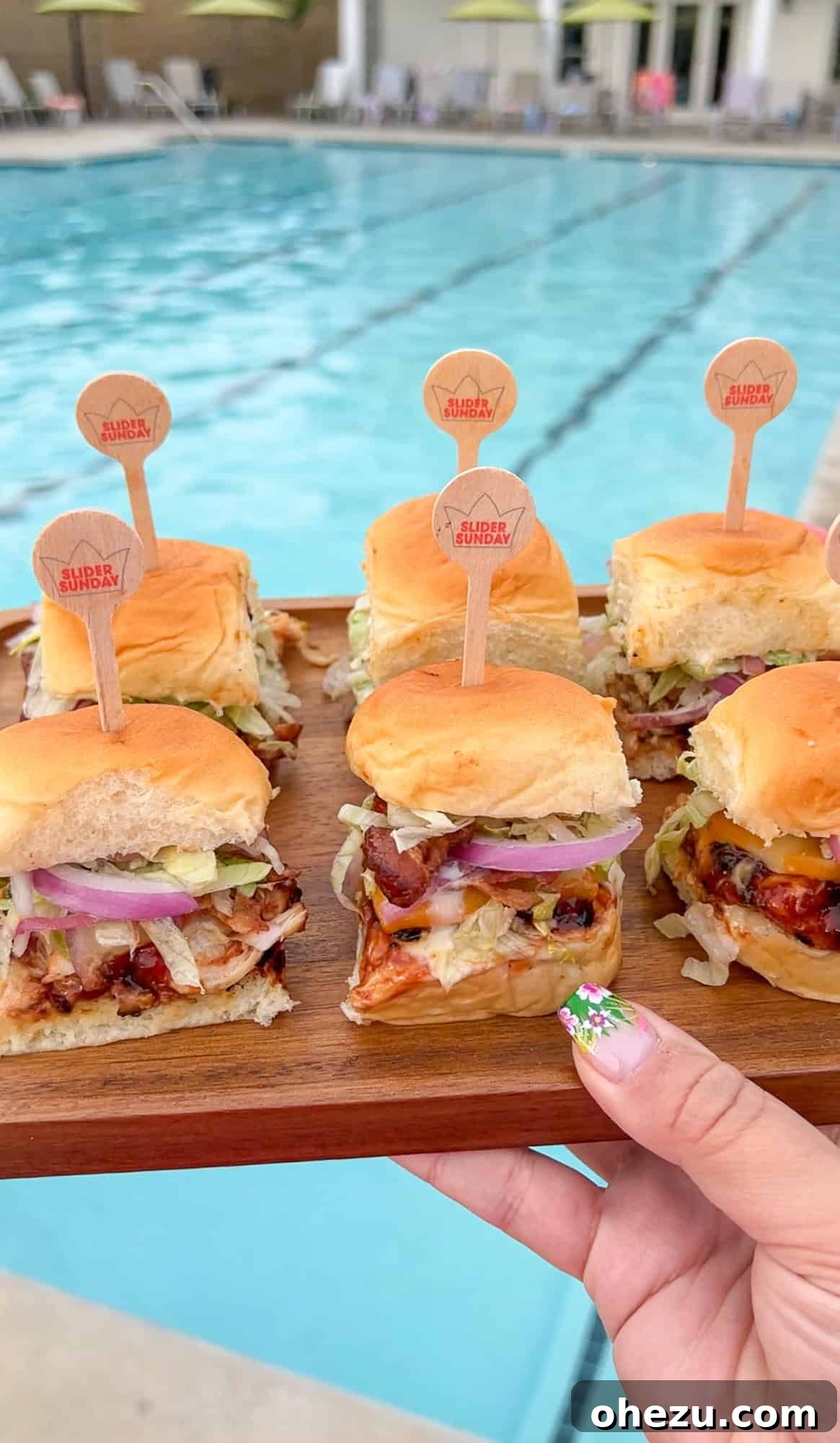 Close-up of a stack of assembled BBQ Chicken Sliders, highlighting layers of chicken, cheese, bacon, and fresh toppings
