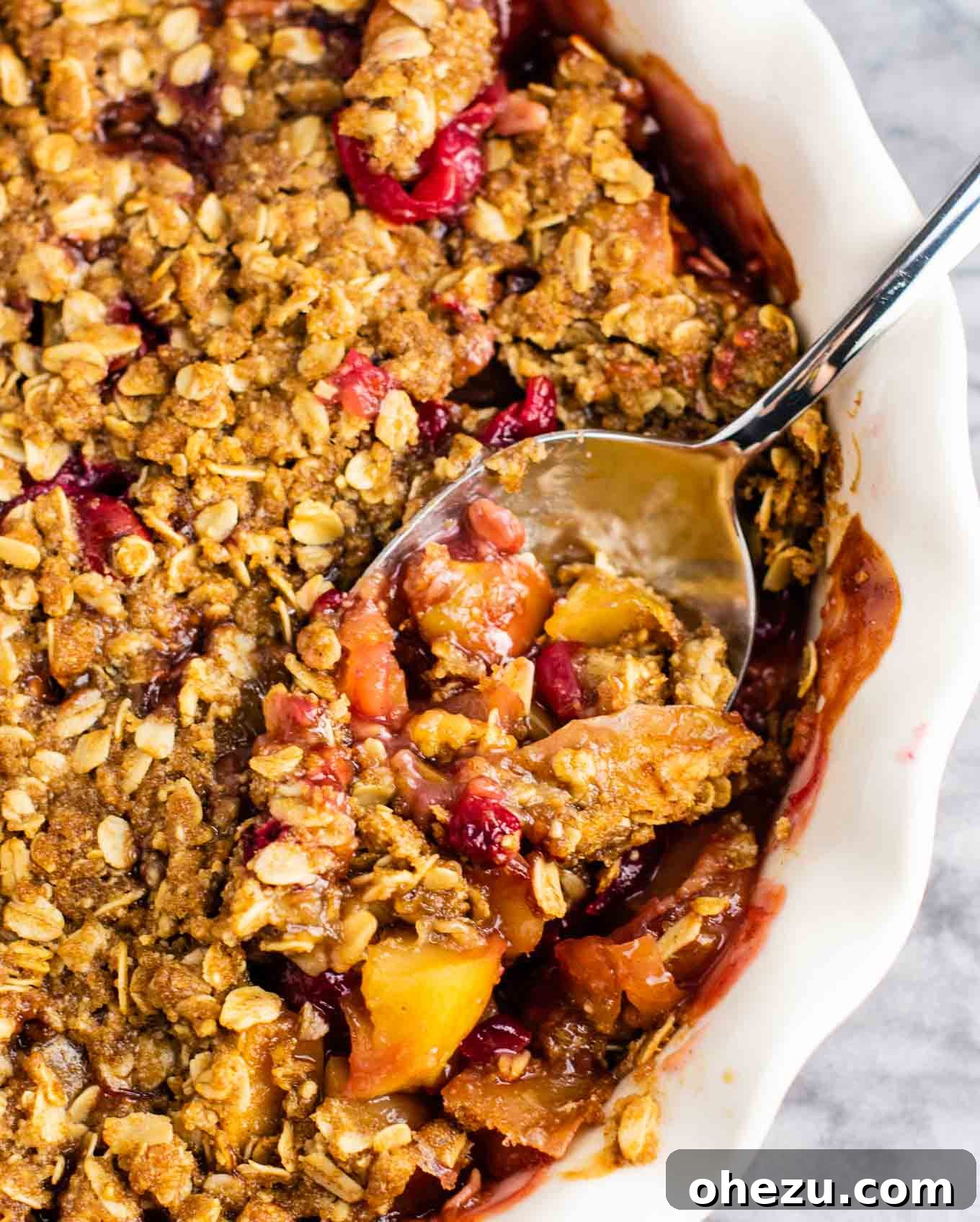 Sweet-Tart Cranberry Apple Crumble 6 A spoon digging into a warm, bubbly Cranberry Apple Crisp, showing the juicy fruit and crunchy topping.