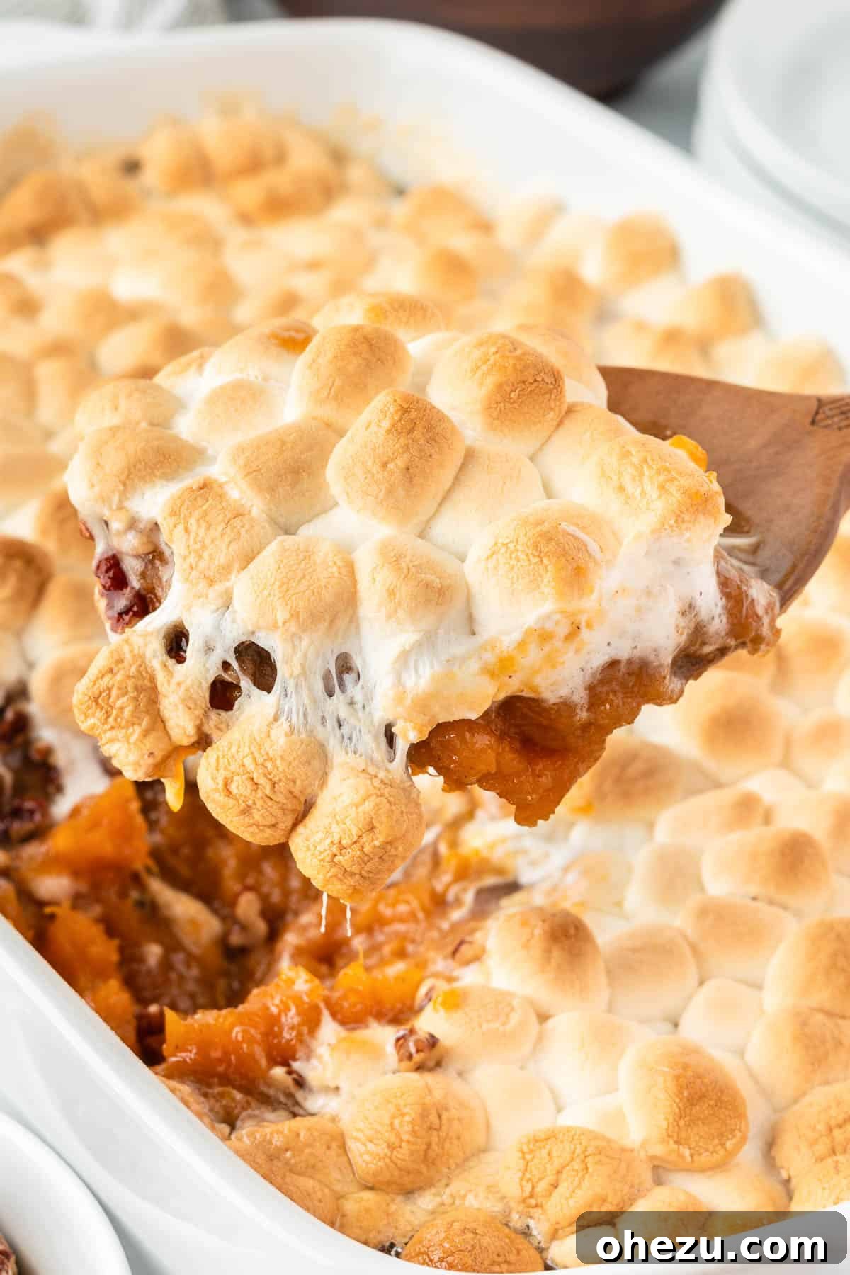36 Scrumptious Vegetarian Thanksgiving Dishes 6 A serving spoon scooping creamy sweet potato casserole from a dish, revealing a delicious marshmallow topping.