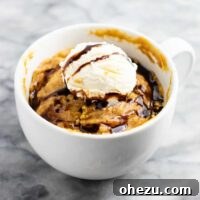 A single serving microwave peanut butter cookie in a mug, golden brown and ready to eat. It's gluten-free, dairy-free, and refined sugar-free, making for a quick and satisfying dessert.