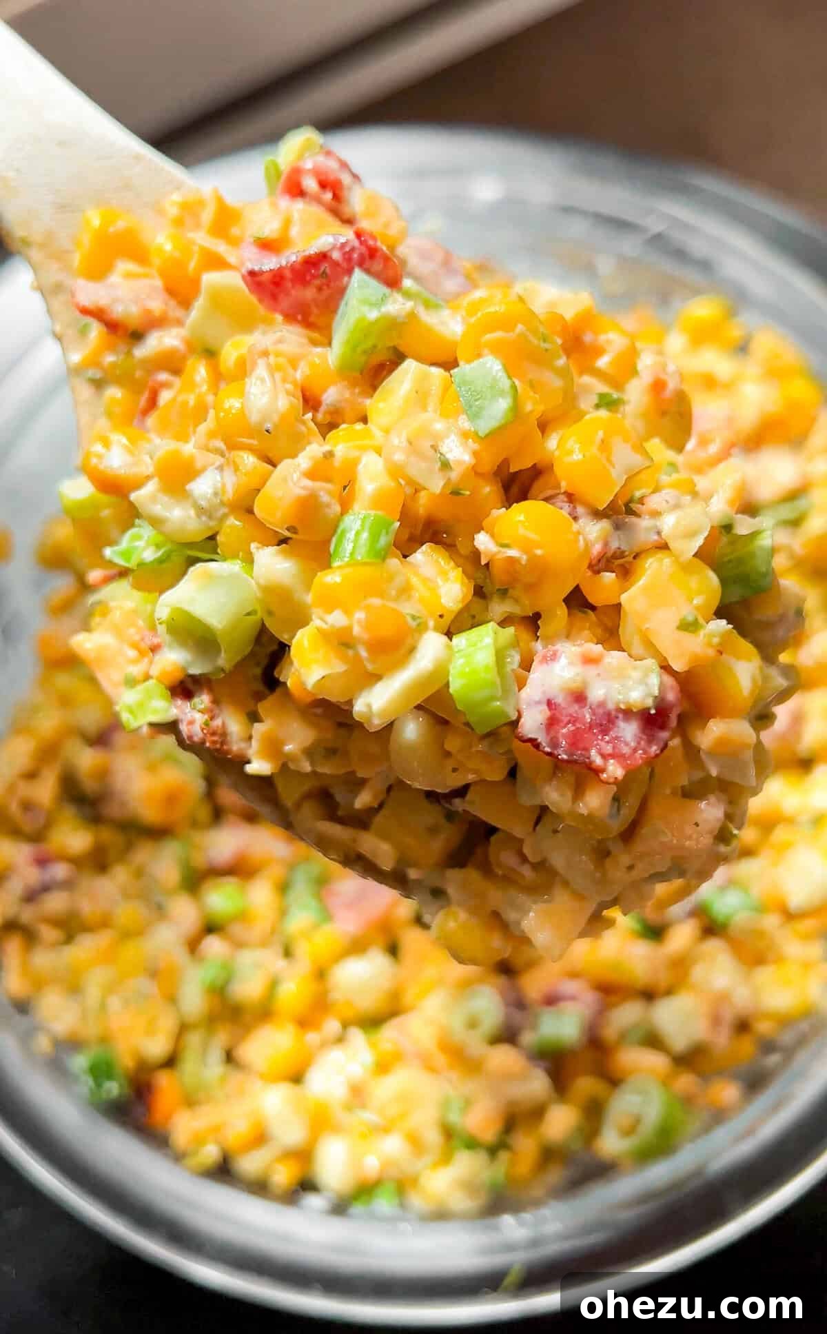 Overhead view of Crack Corn Salad in a white bowl, garnished with green onions and bacon bits, ready to serve.