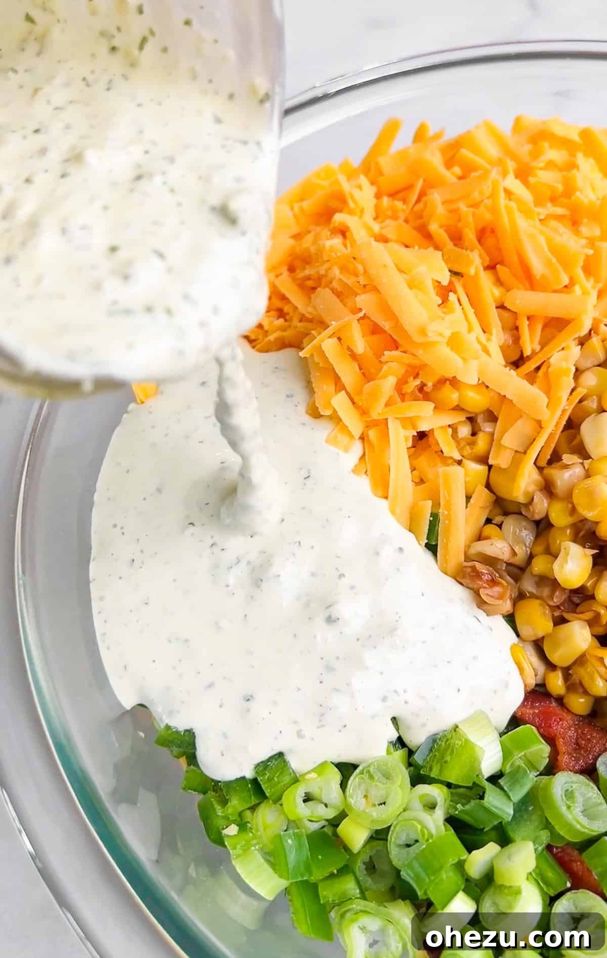 A large white bowl filled with Crack Corn Salad, showing corn, bacon, cheese, and dressing mixed together.