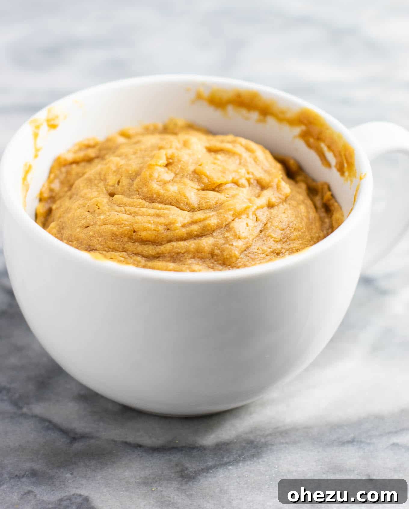 A freshly microwaved gluten-free, dairy-free, and refined sugar-free peanut butter cookie in a mug, showcasing its soft, cake-like texture, ready to be enjoyed.