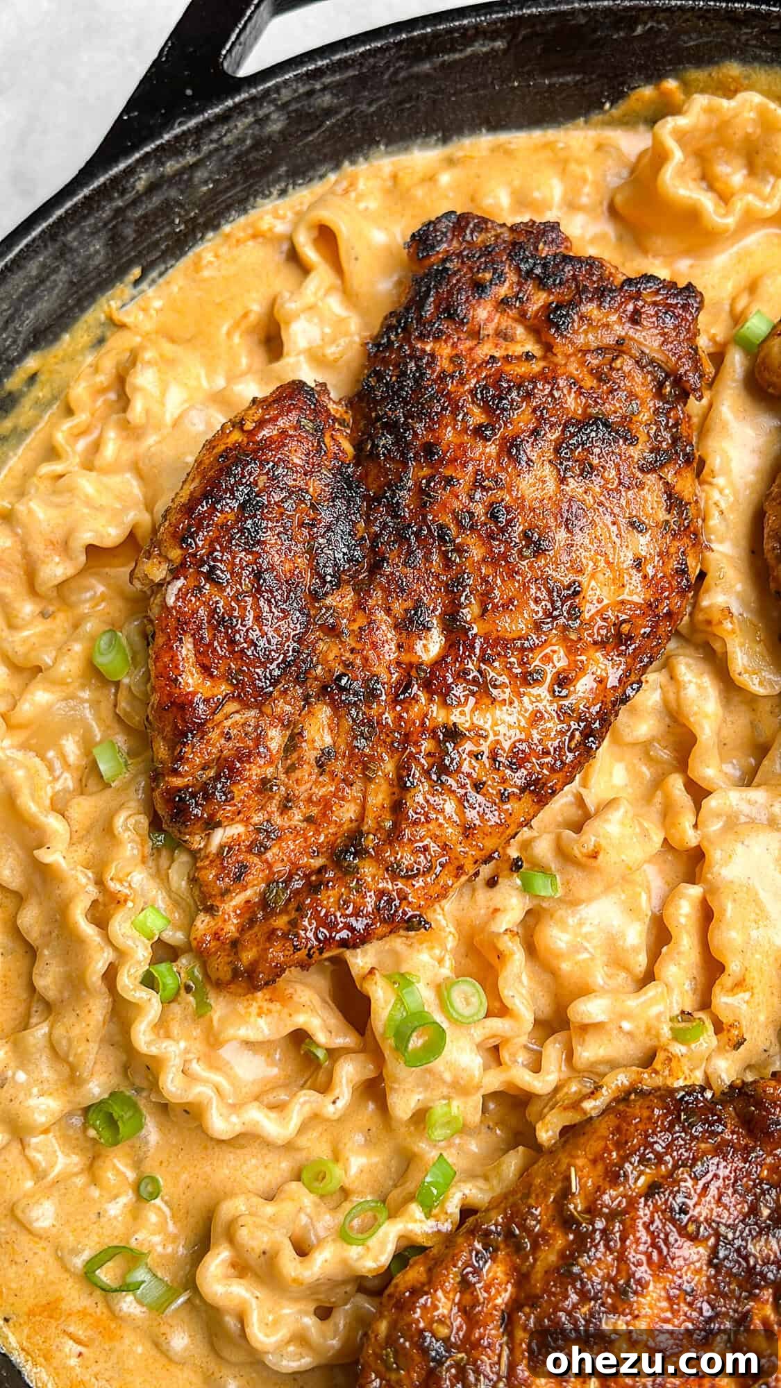 A cook stirring long pasta noodles directly into a rich, creamy sauce in a large pan