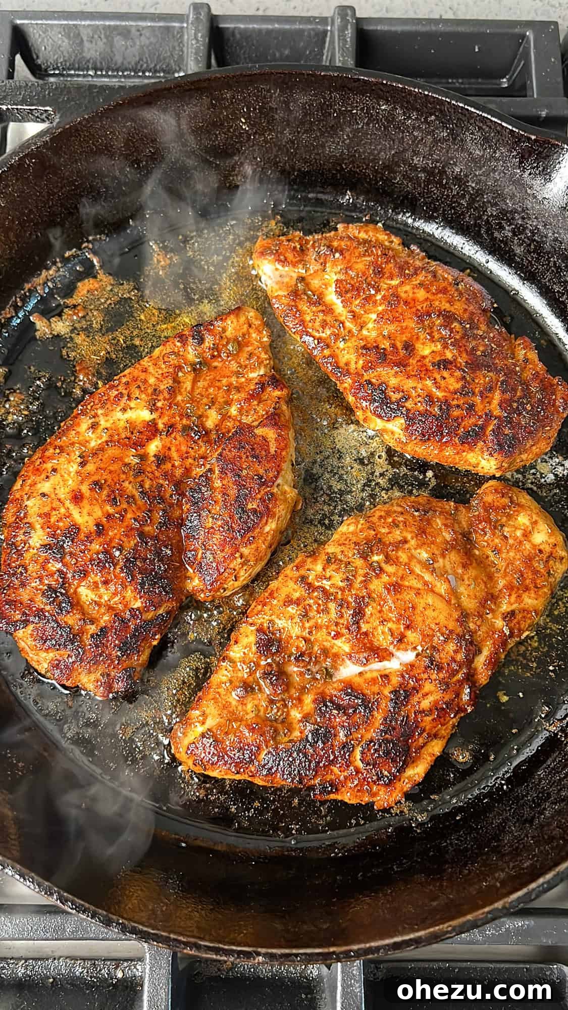 Cajun-seasoned chicken breasts searing in a hot skillet with olive oil