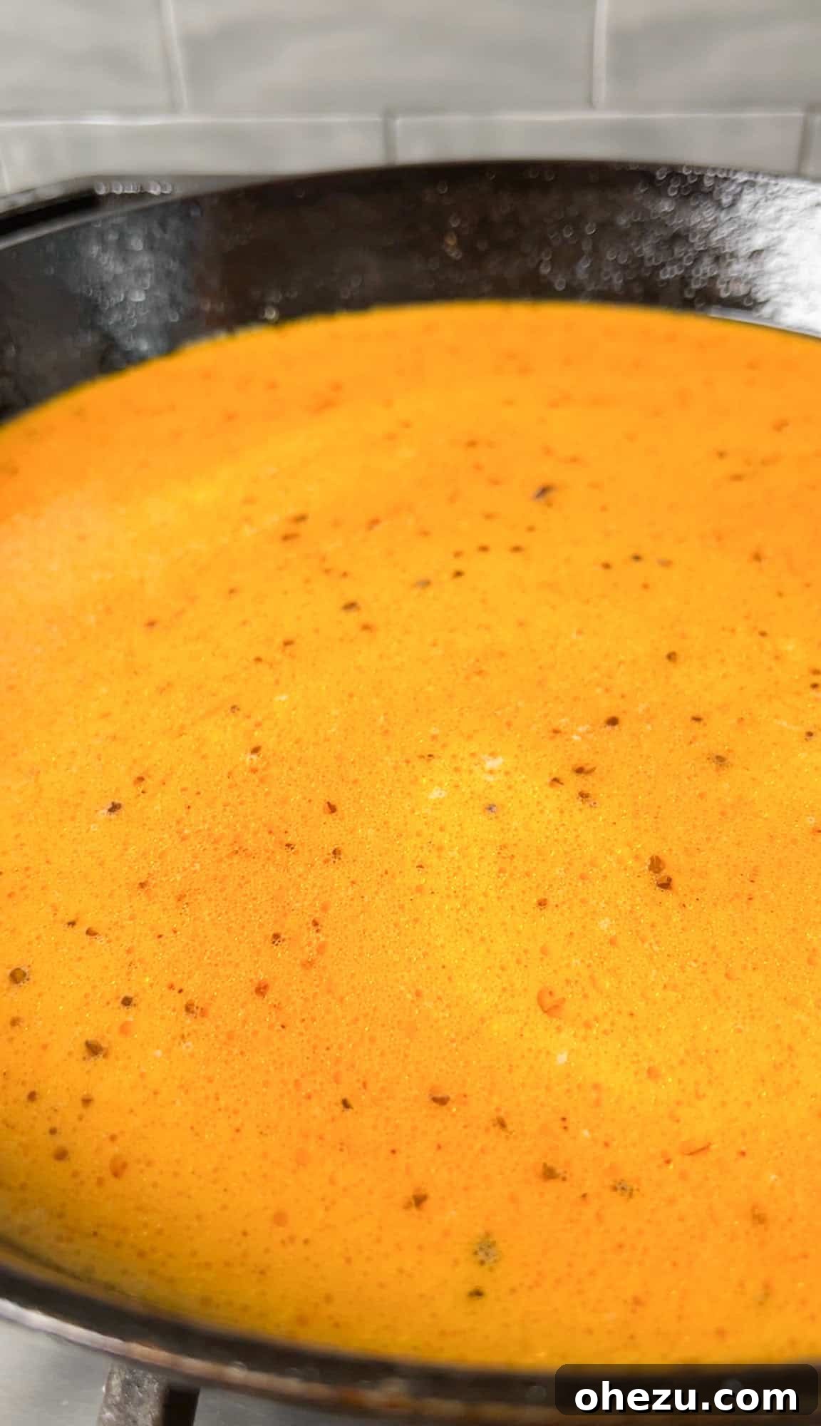 Chicken stock, milk, buffalo sauce, and seasoning simmering in a skillet with garlic and butter